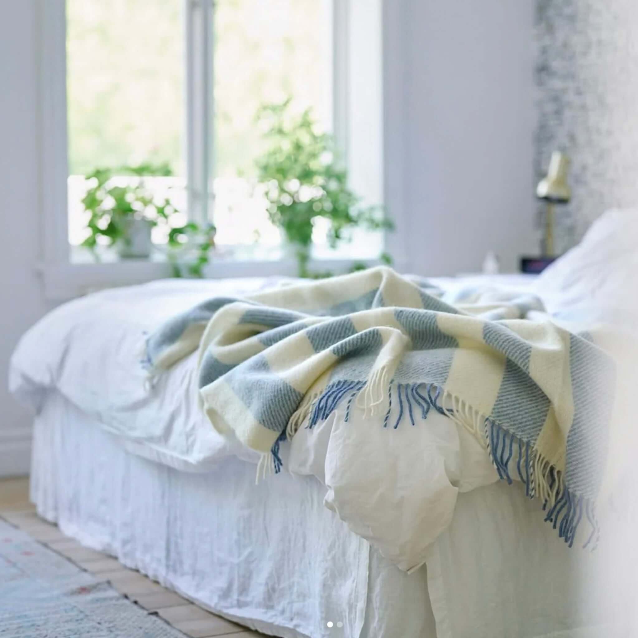 Klippan Yllefabrik Gotland Wool Vertical Stripe Throw - Heavenly Blue & White draped on a bed with greenery.