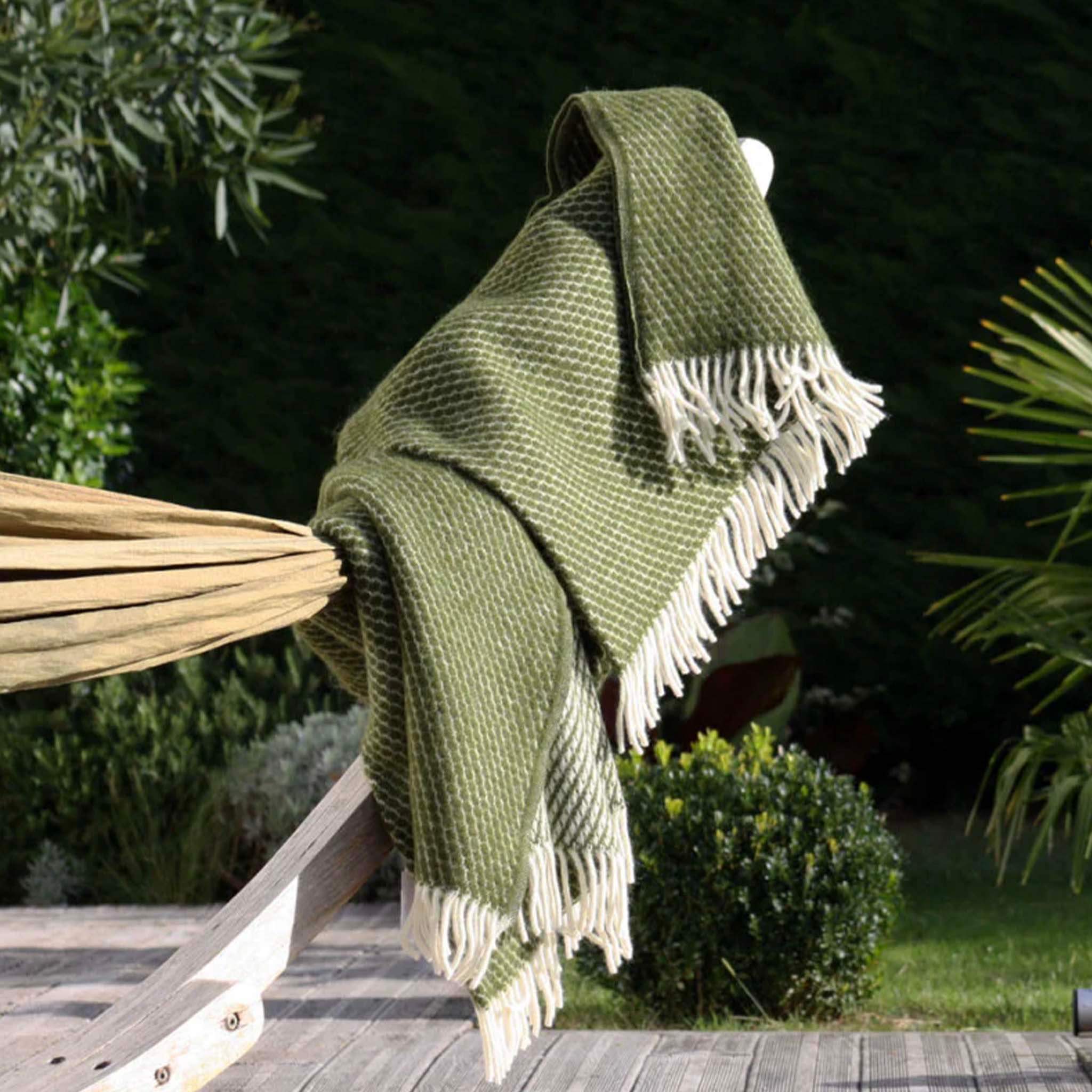 Klippan Yllefabrik Velvet Lambswool Throw - Avocado draped on a chair outdoors, showcasing its soft texture and cream fringe trim.