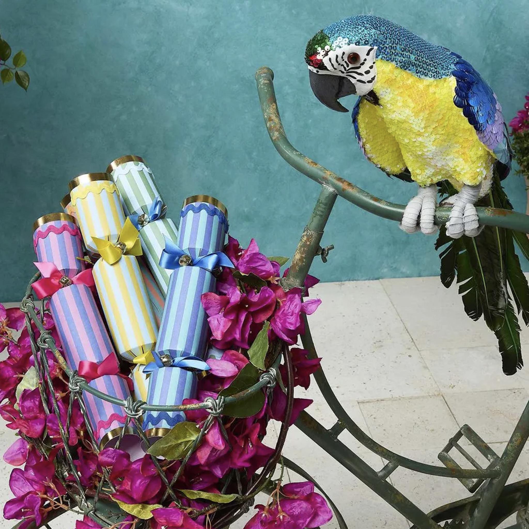 Colorful parrot perched on a metal chair with decorative eggs and flowers against a teal background