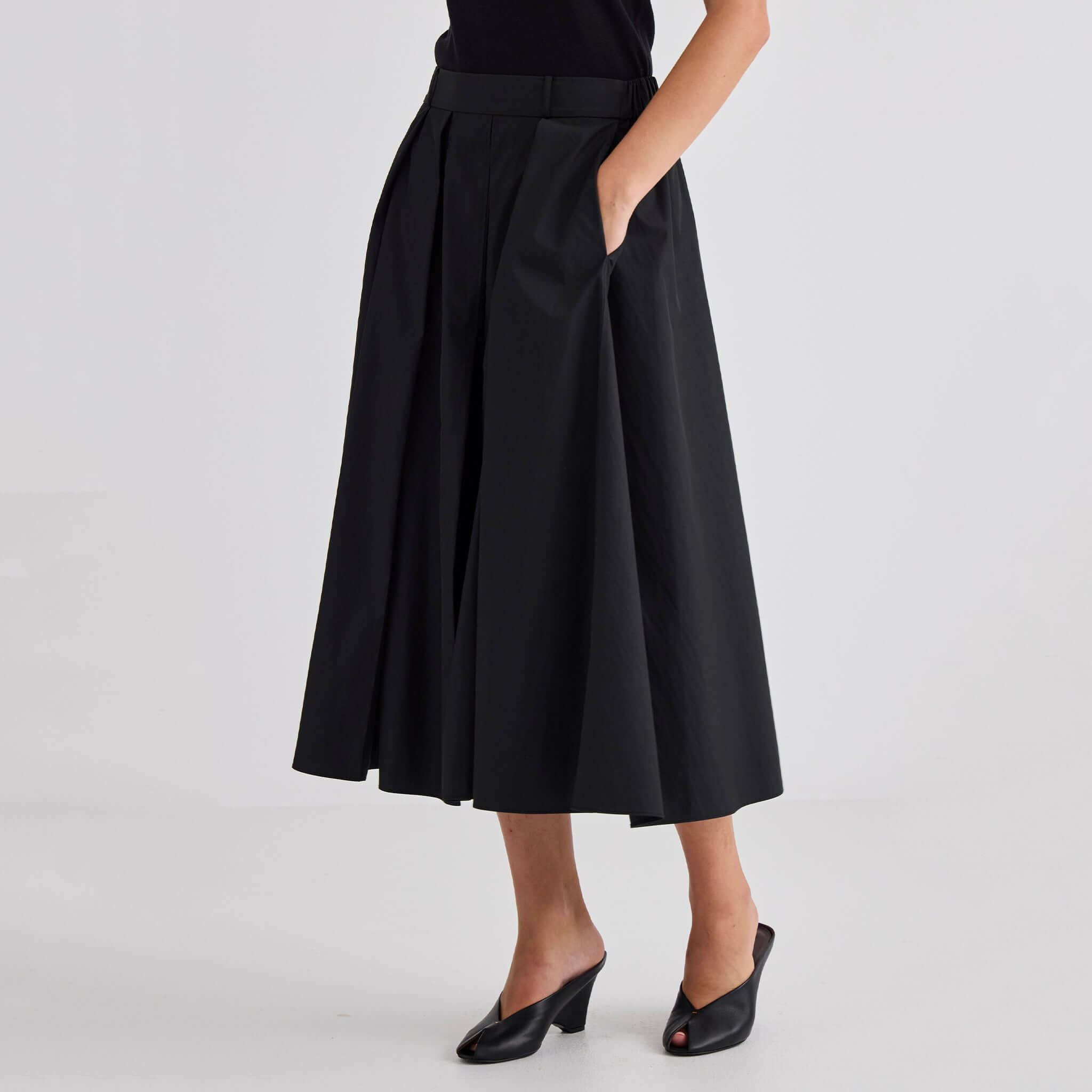 Laing Ellis Pleated Skirt - Black featuring deep box pleats and an elasticated waistband, styled effortlessly with heels.