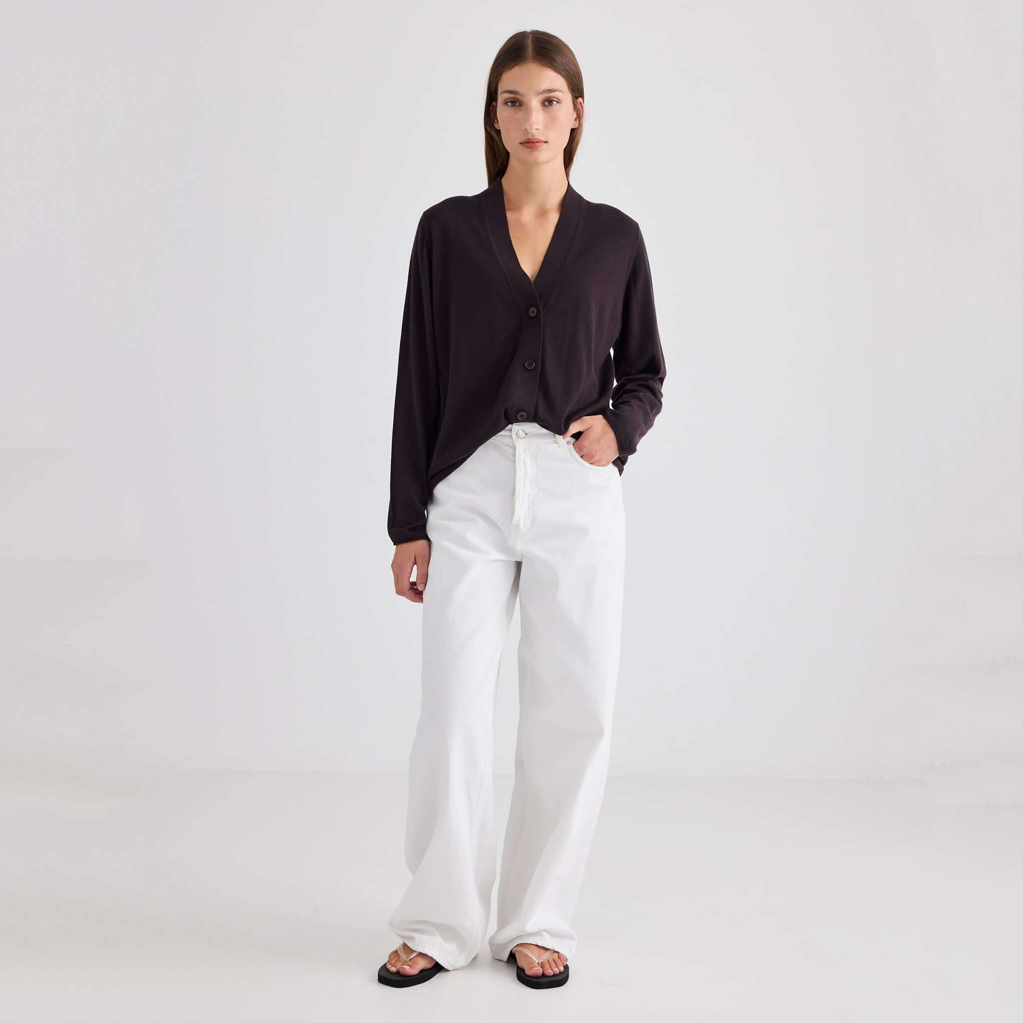 Model wearing Laing Liv V-Neck Merino Cardigan - Chocolate paired with white trousers on light background.