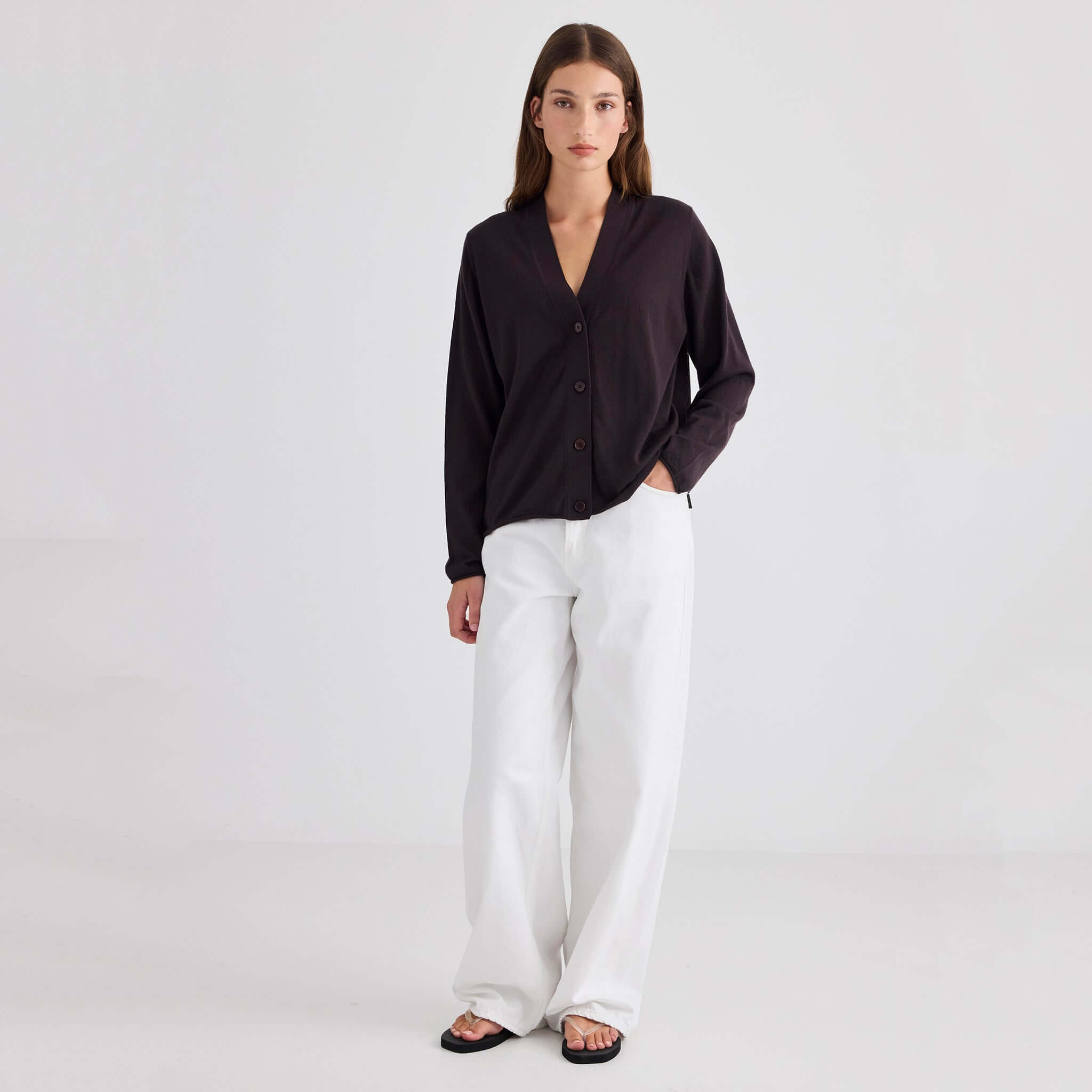 Laing Liv V-Neck Merino Cardigan - Chocolate worn with white pants in a minimalist setting.
