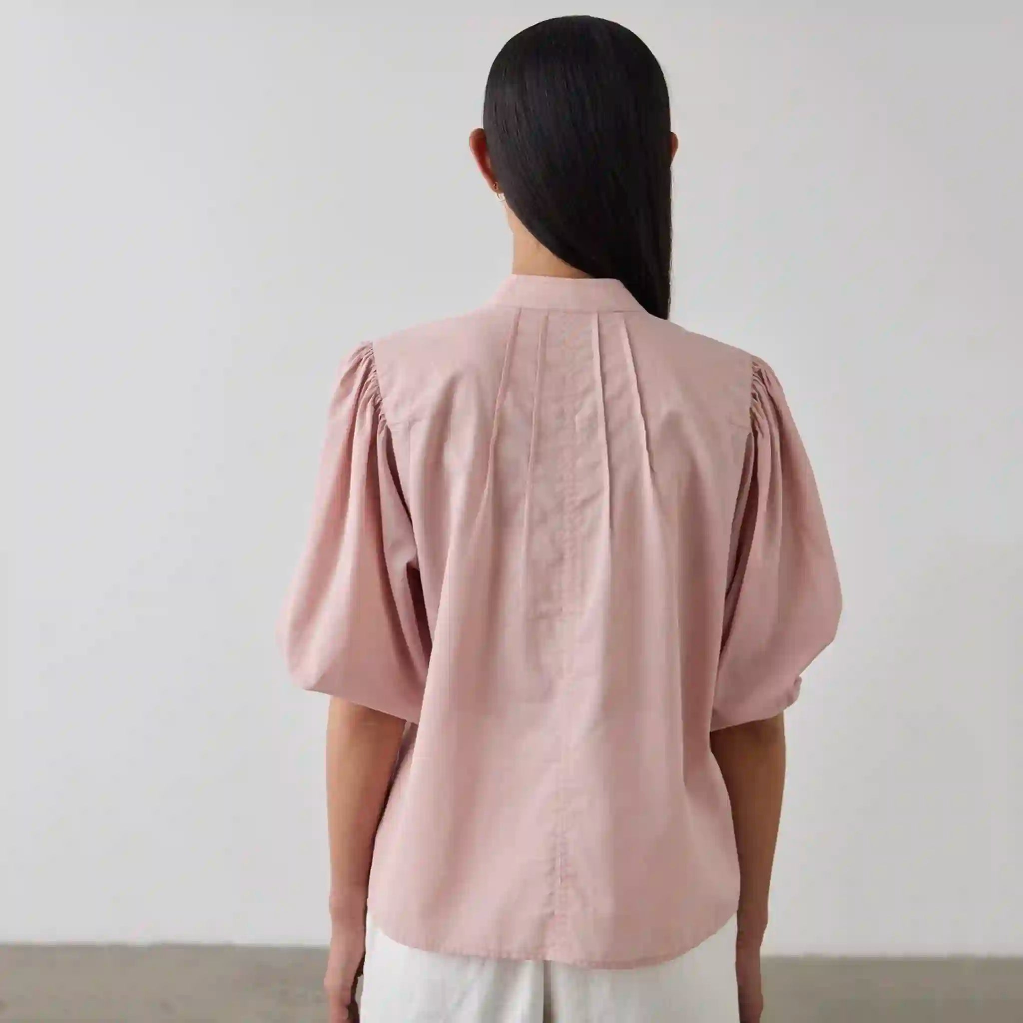 Person wearing a light pink blouse with puff sleeves against a plain background