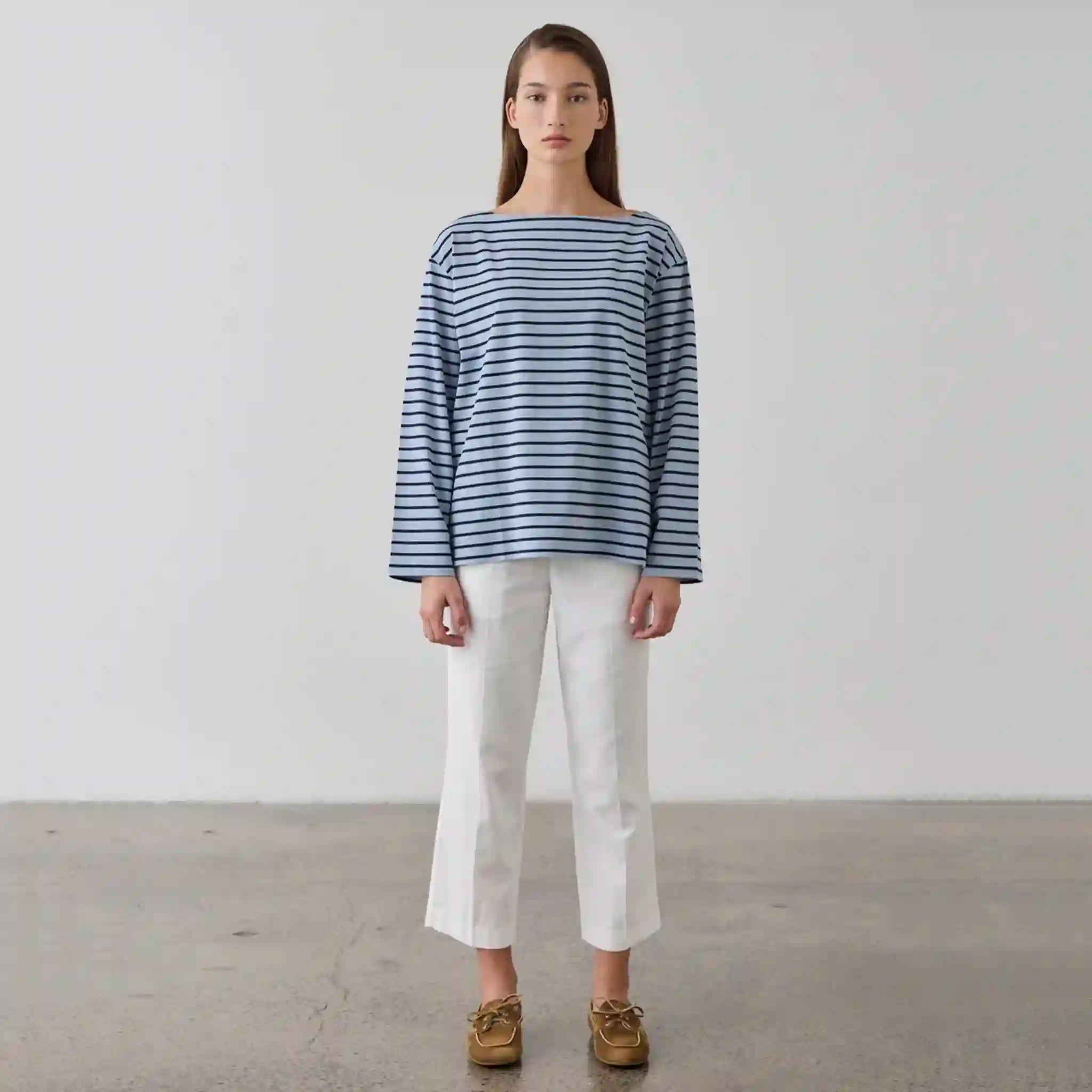 Person wearing a blue and white striped shirt with white pants against a plain background