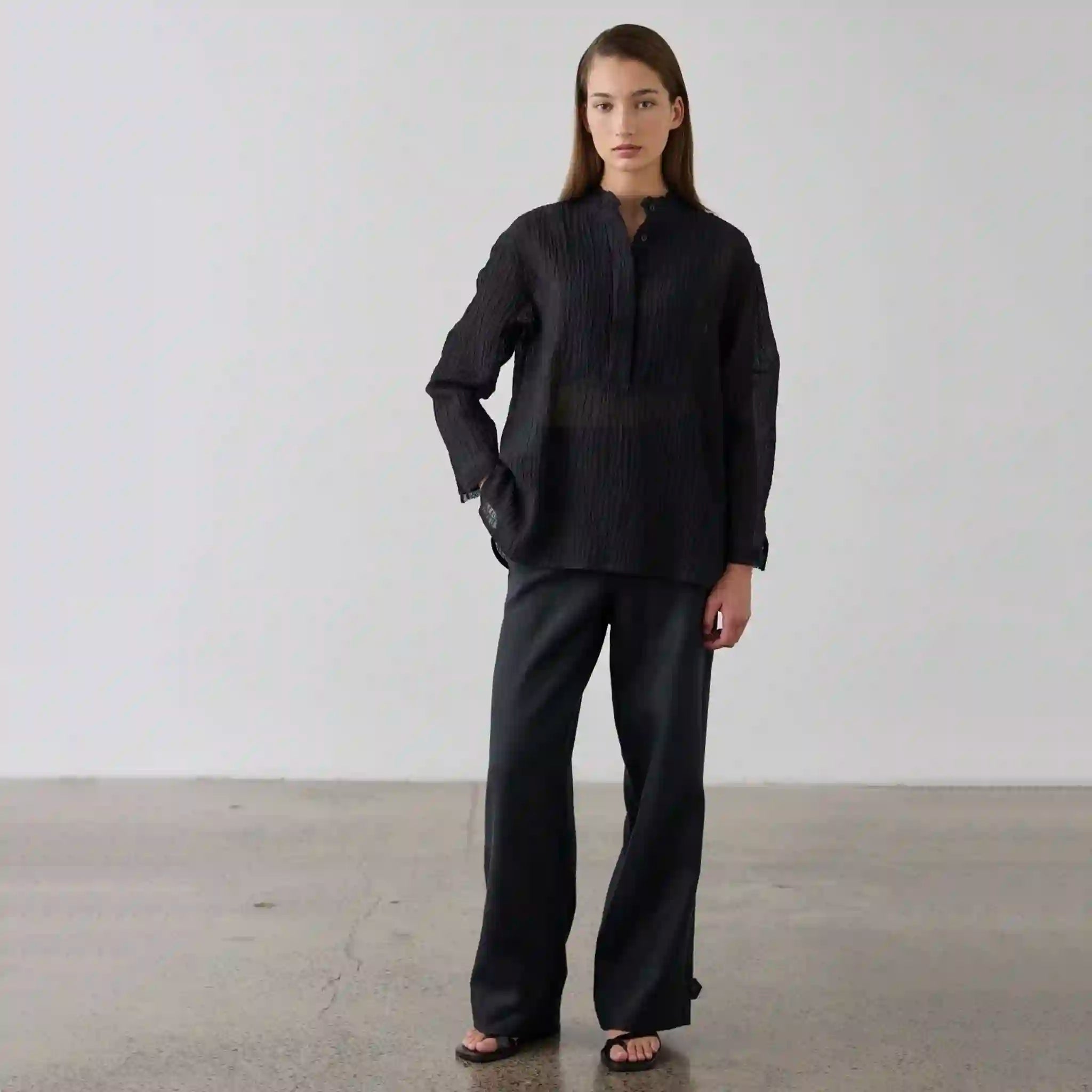 Person wearing a black outfit standing against a plain background