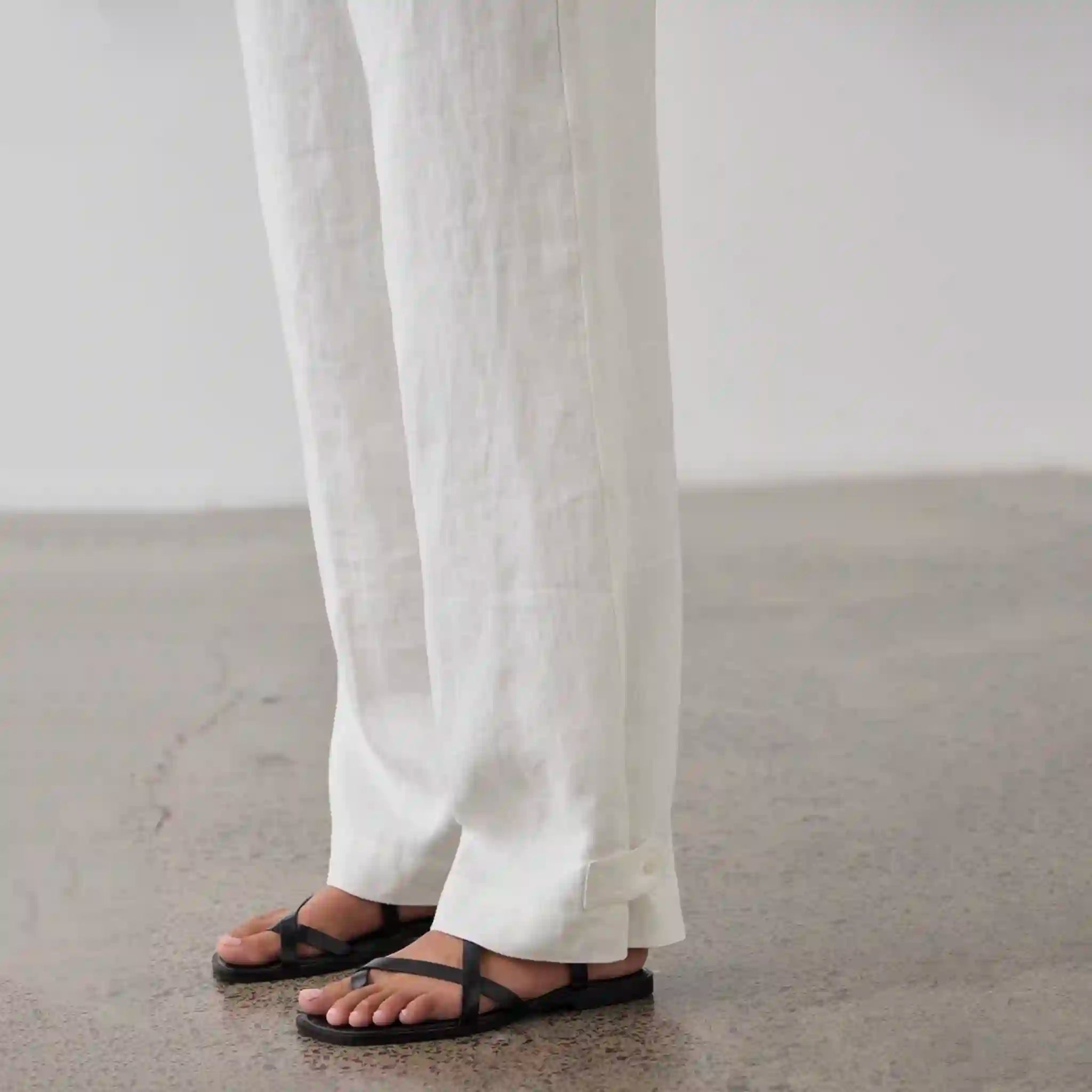 Person wearing white pants and black sandals on a neutral background