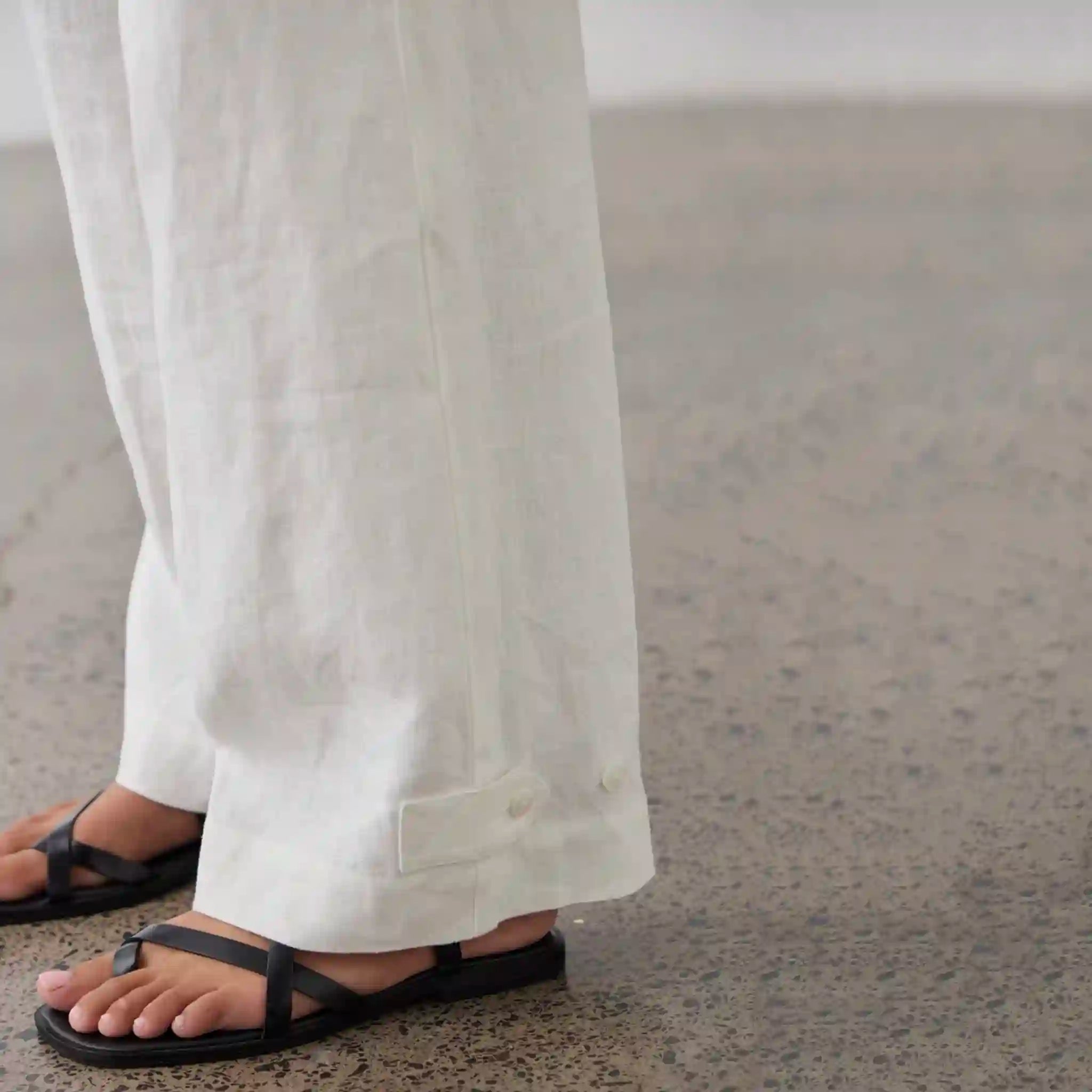 Person wearing white pants and black sandals on a neutral background