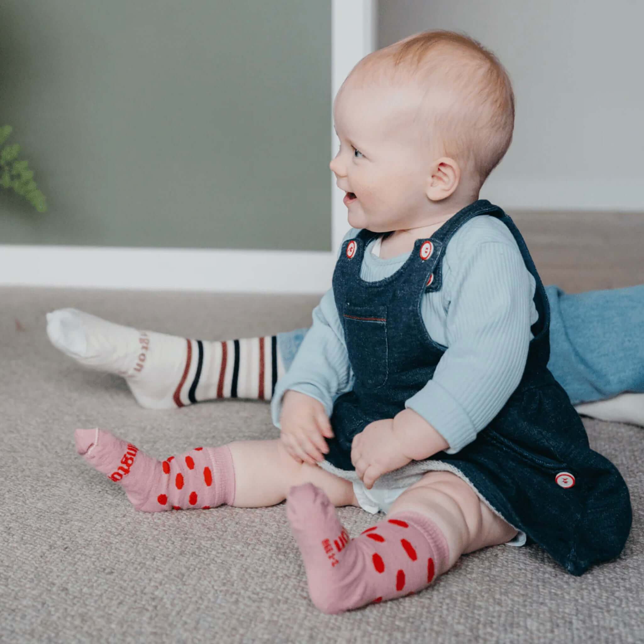 Lamington Merino Crew Baby Socks - Cherry worn by a smiling baby, showcasing playful polka dot design.