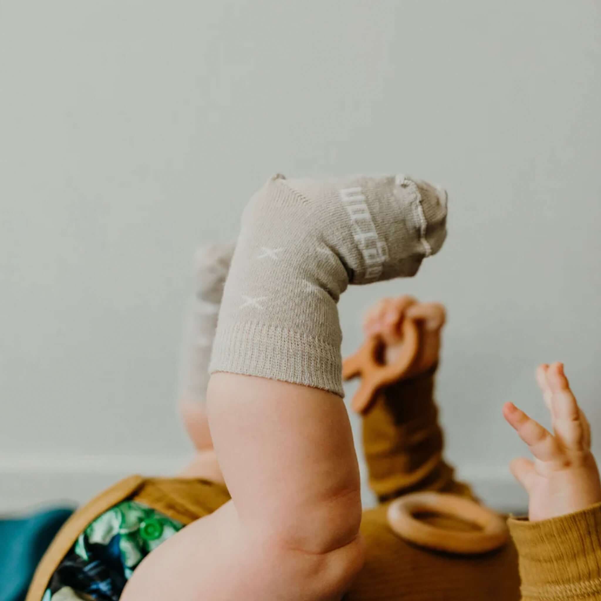 Lamington Merino Crew Baby Socks - Ted on a baby's feet, featuring warm oat color and white cross motifs.