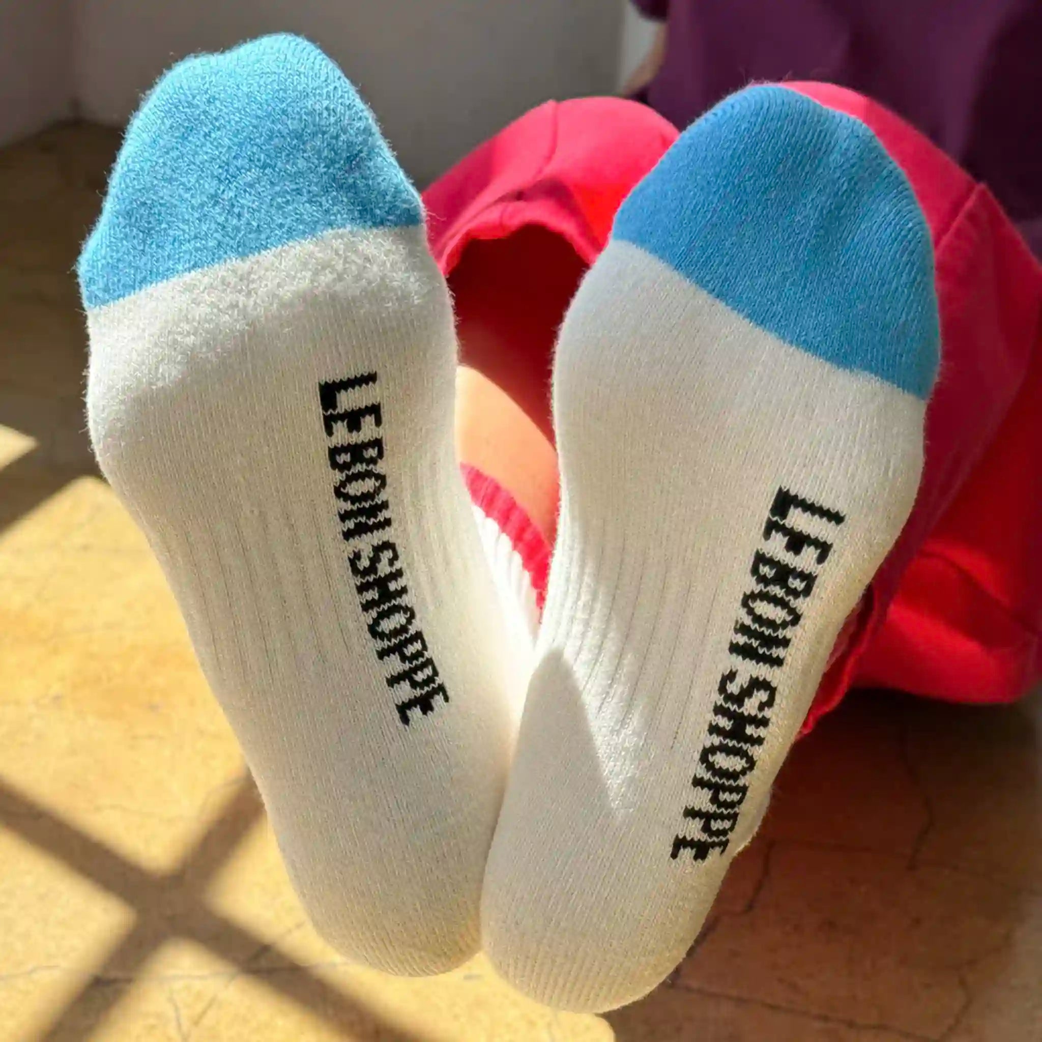 White socks with blue toes and soles, labeled 'Le Bon Shoppe', worn by a person in red pants.
