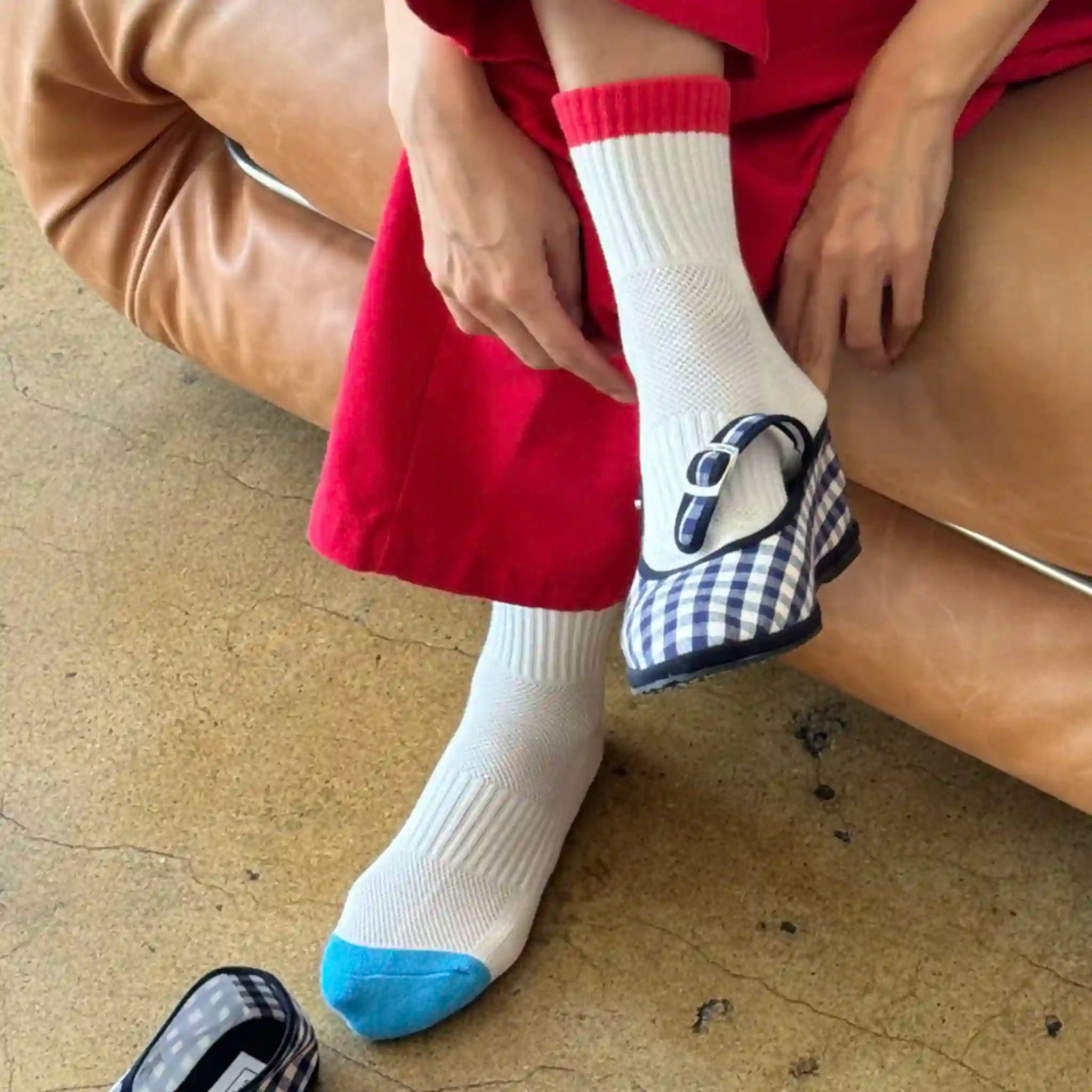 Person wearing a red dress and white socks with blue accents, sitting on a brown leather couch.