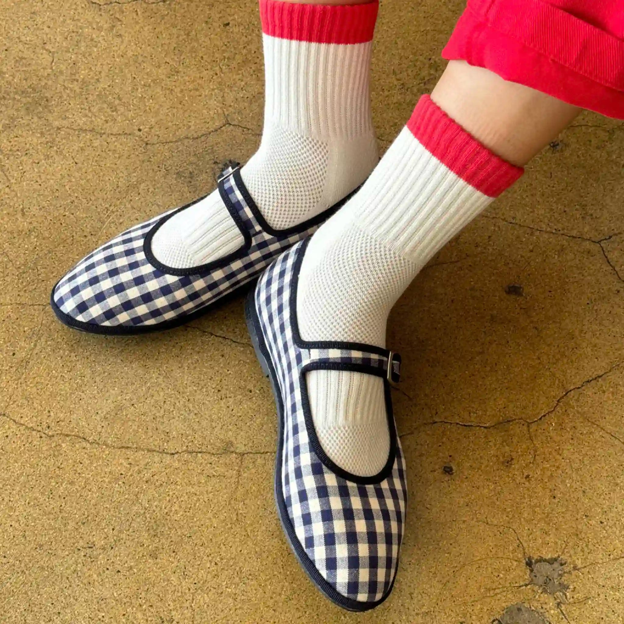 Blue checkered shoes worn with white socks and red trim on a beige surface
