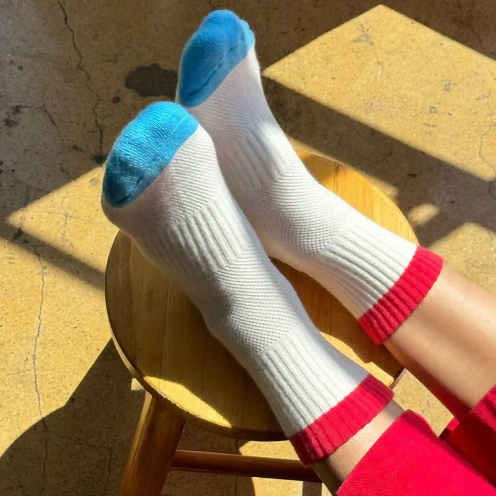 White socks with blue toes and red cuffs on a wooden stool.