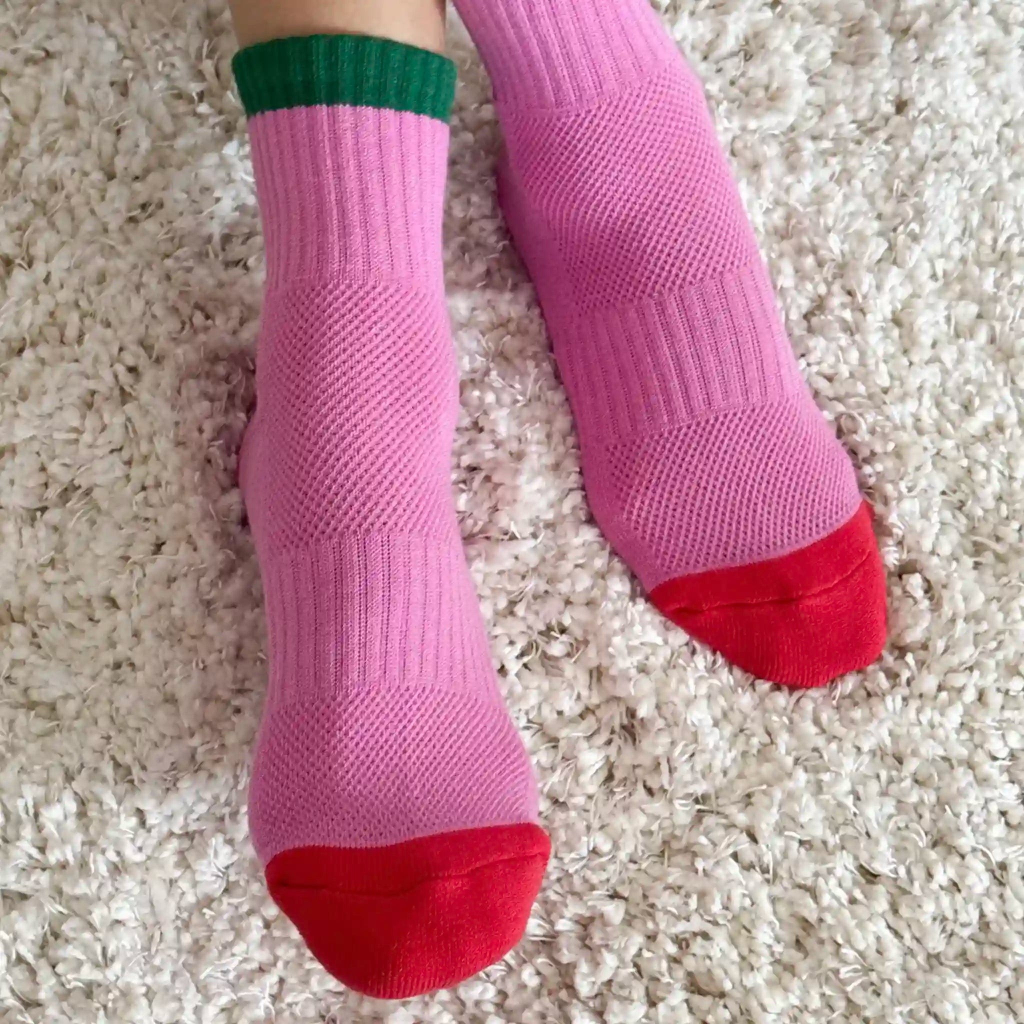 Pink socks with green cuffs and red toes on a beige carpet