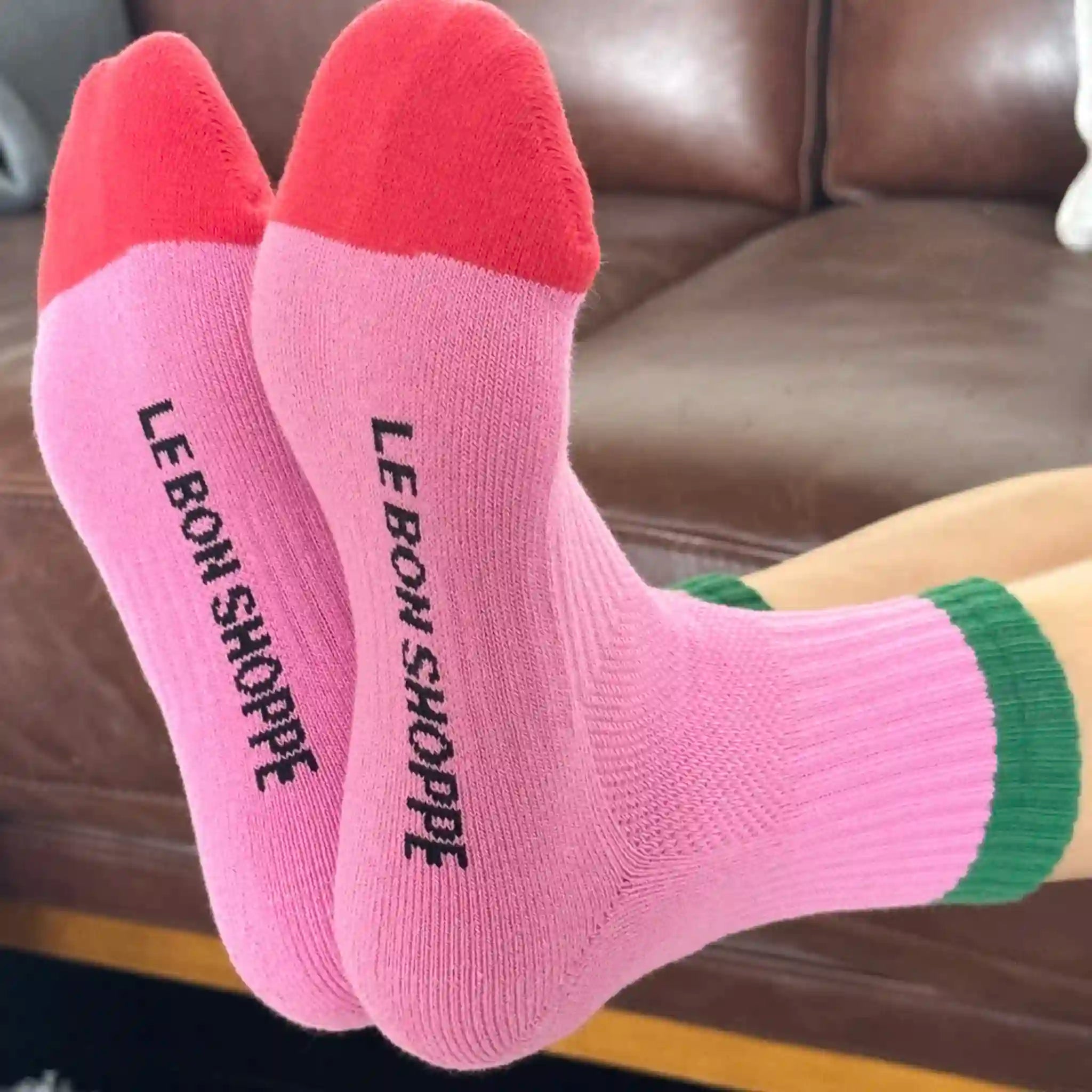 Pink socks with 'LE BON SHOPPE' branding on a brown leather couch.