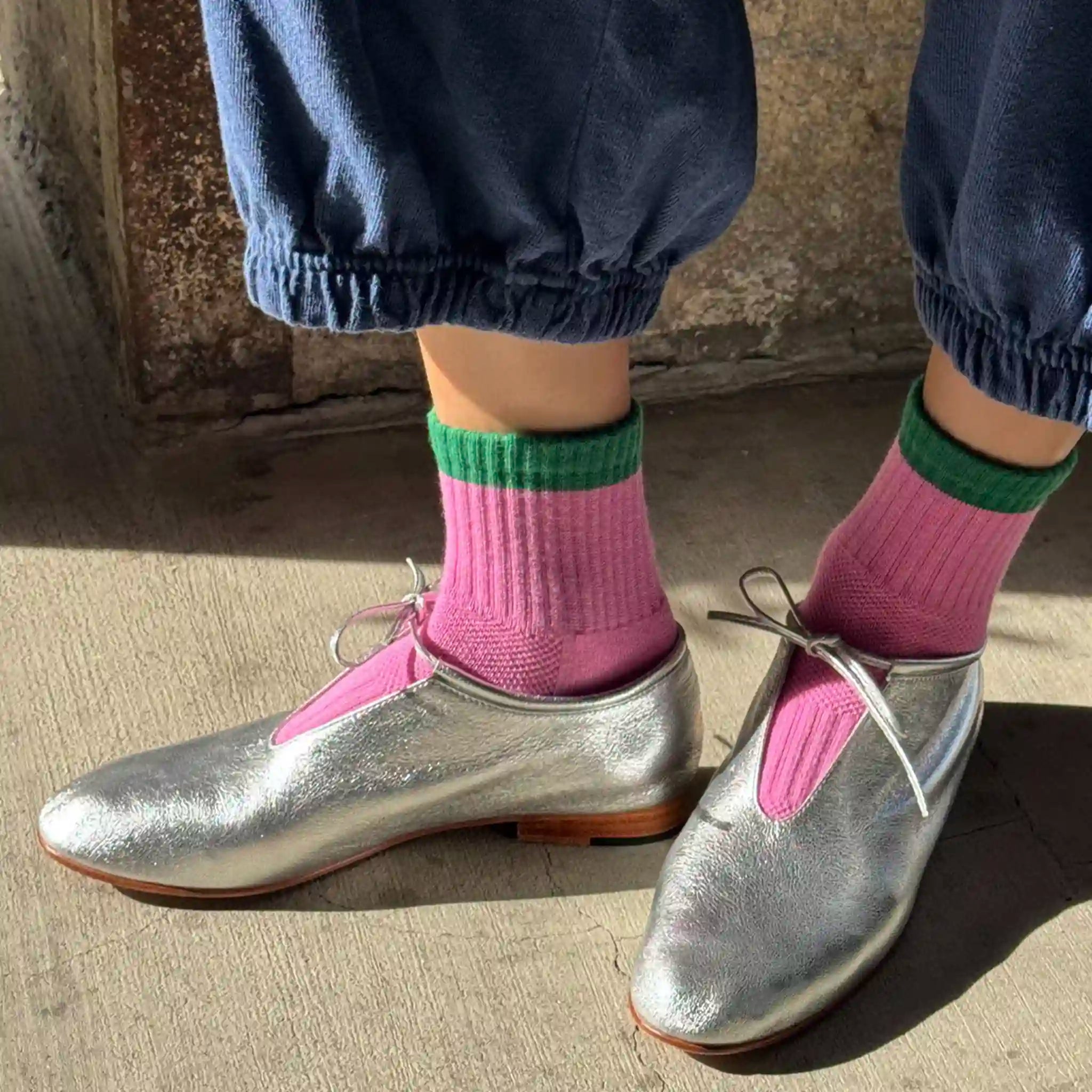 Silver shoes with pink accents worn with purple socks and green cuffs on a concrete surface.