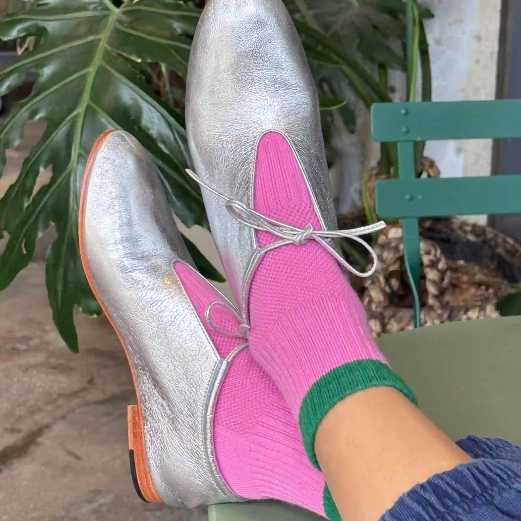 Silver shoes with pink socks and green cuffs worn by a person sitting on a bench.