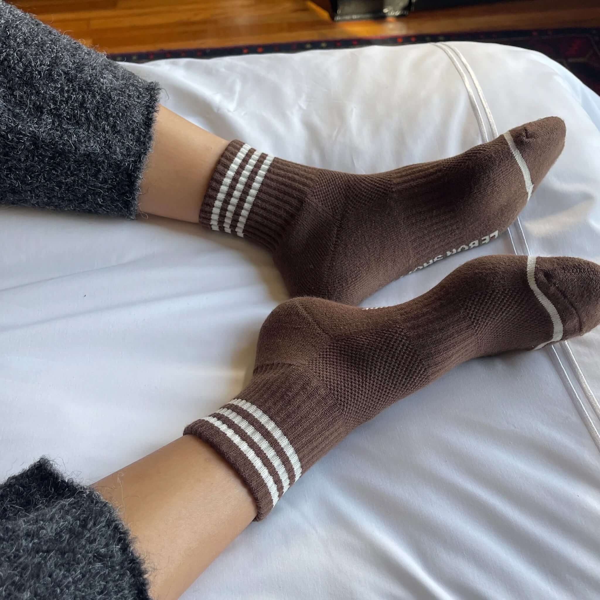 Le Bon Shoppe Girlfriend Socks - Mahogany worn on cozy bed, showcasing triple contrast stripe and classic crew design.