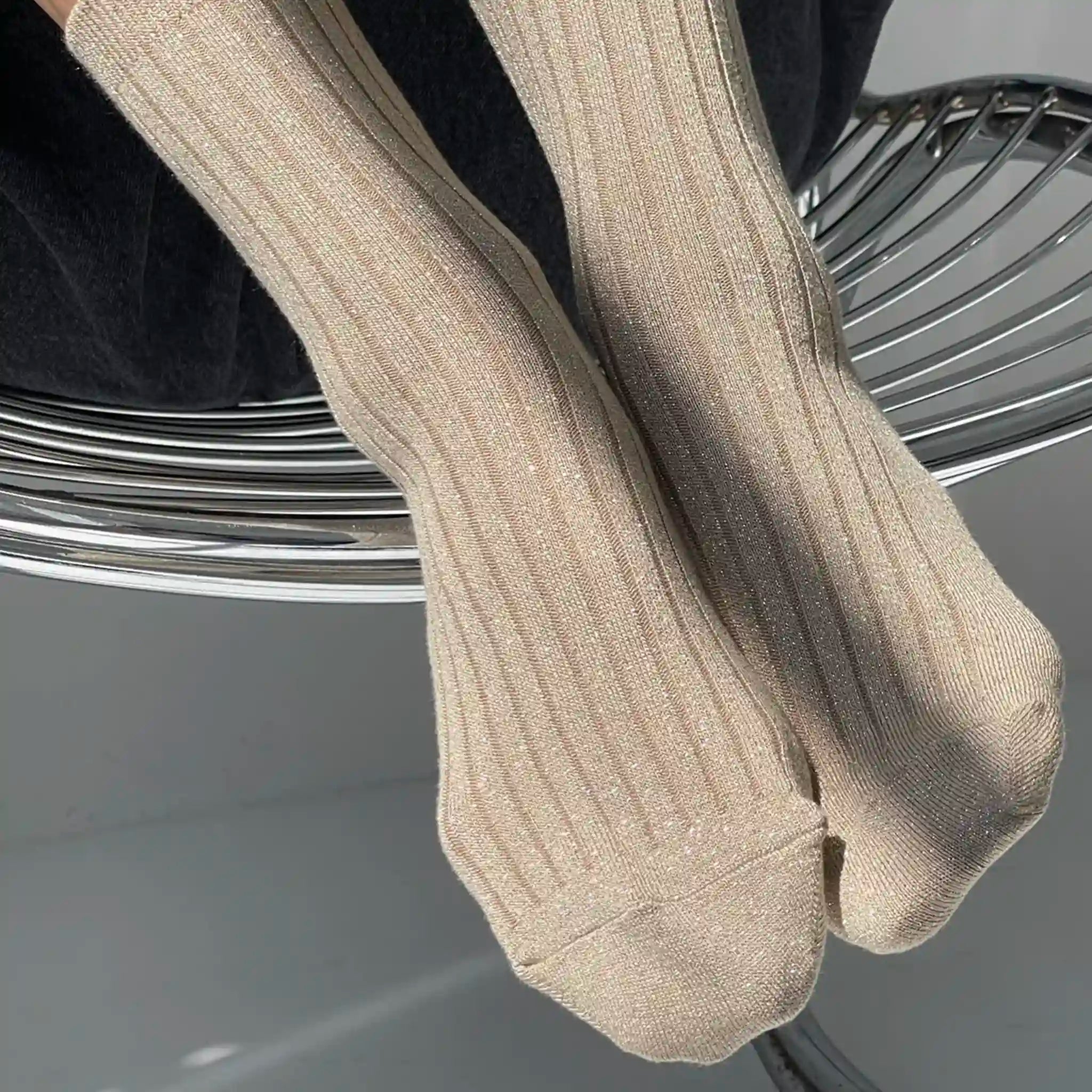 Beige ribbed socks worn by a person sitting on a metal chair.