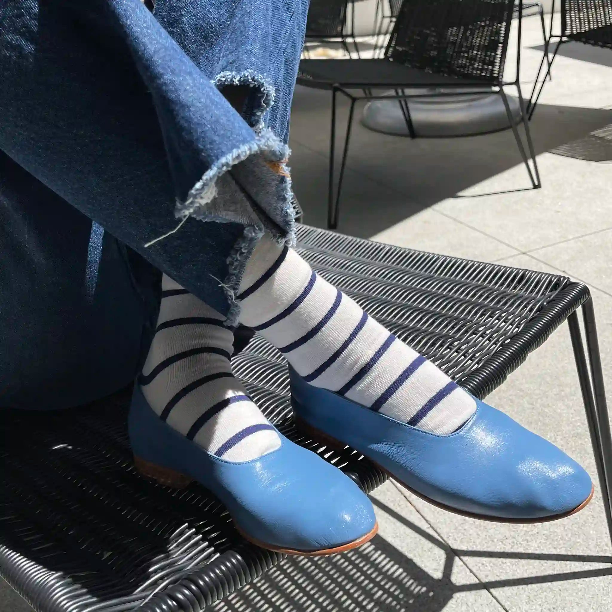 Person wearing blue shoes and striped socks sitting on a metal chair outdoors.