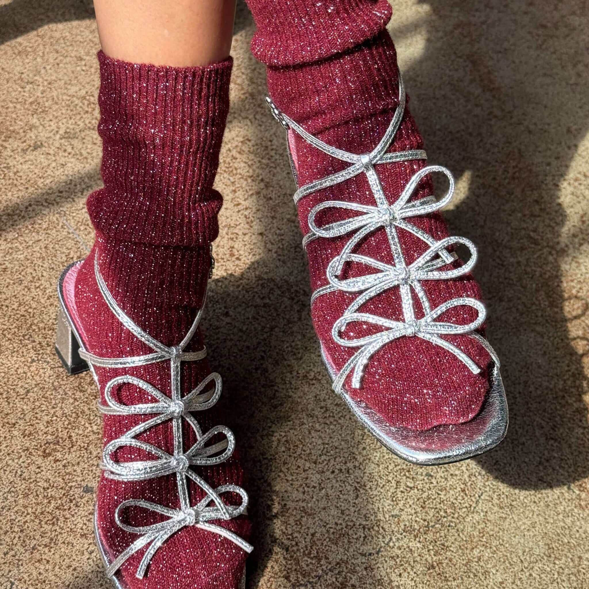 Le Bon Shoppe Winter Sparkle Socks - Wine paired with stylish silver strappy heels on a textured surface.