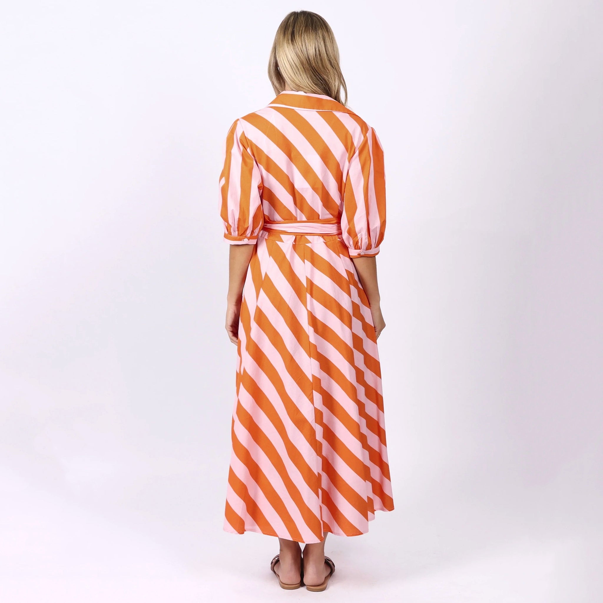 Woman wearing a long orange and white striped dress on a white background