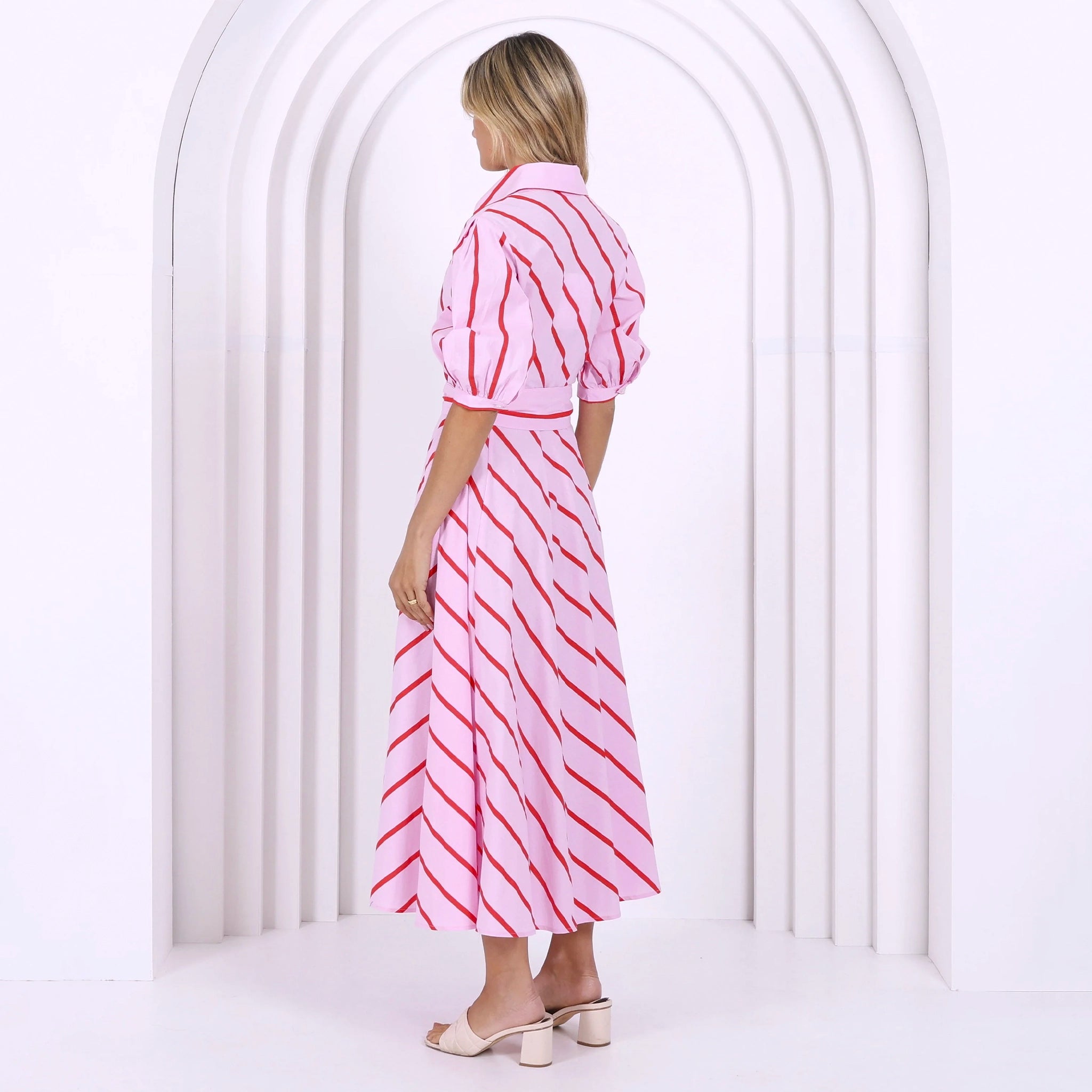 Woman wearing a pink and white striped dress standing in front of a white archway.