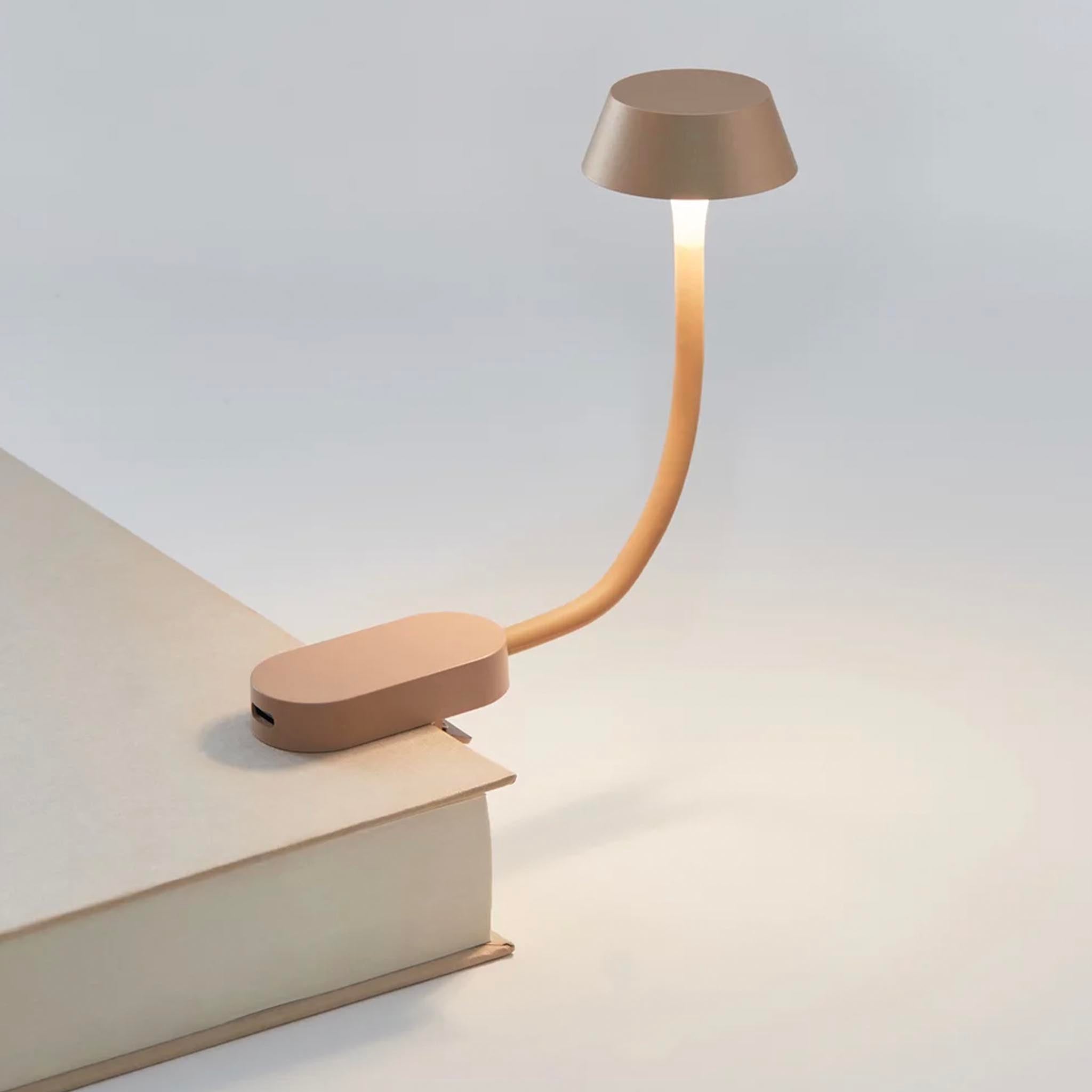 Beige LED reading lamp with flexible arm on a book against a light gray background