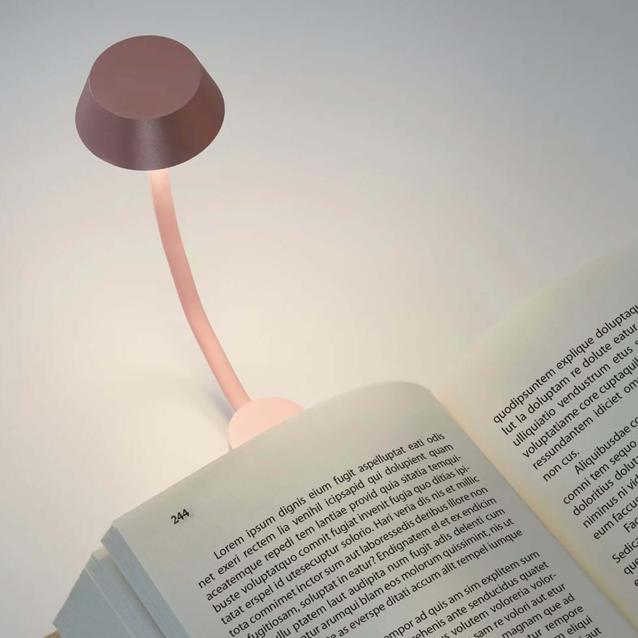 Lexon Mimi Clip-on Reading Lamp - Light Pink illuminating an open book with its stylish design and warm LED light.