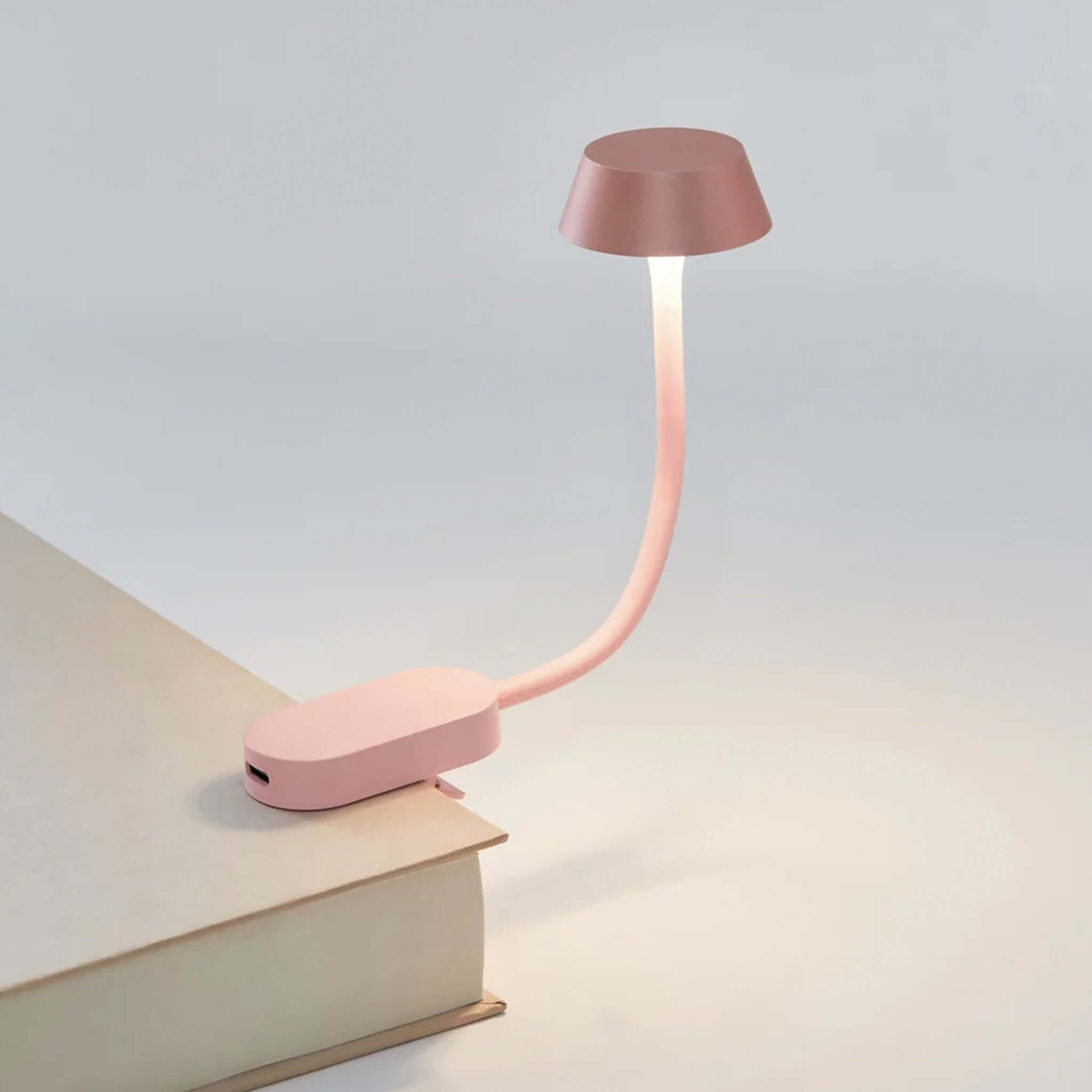 Lexon Mimi Clip-on Reading Lamp - Light Pink illuminating a book with its elegant design.