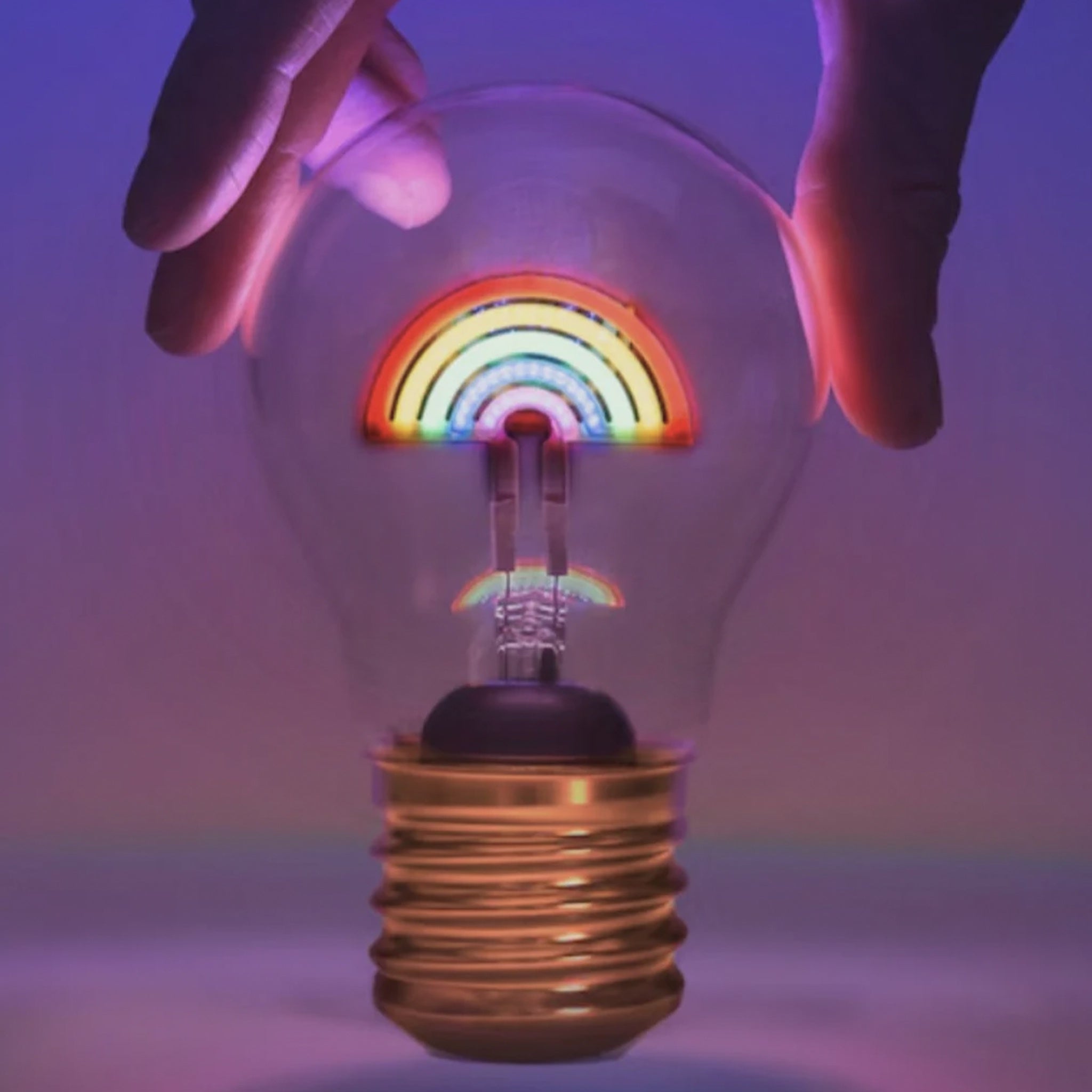 Light bulb with rainbow inside held by hands against a gradient background