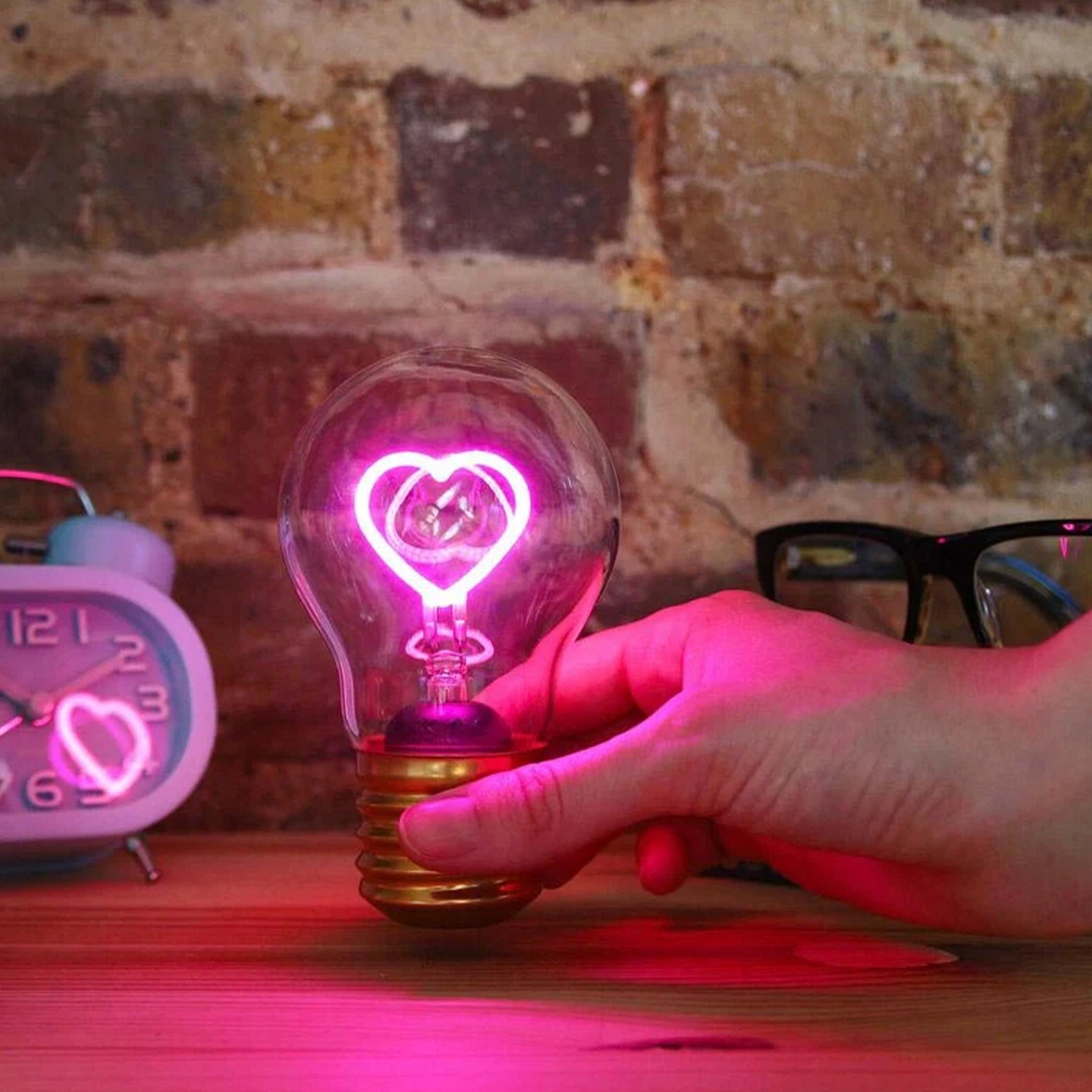 Light bulb with heart shape inside held by a hand against a brick wall background
