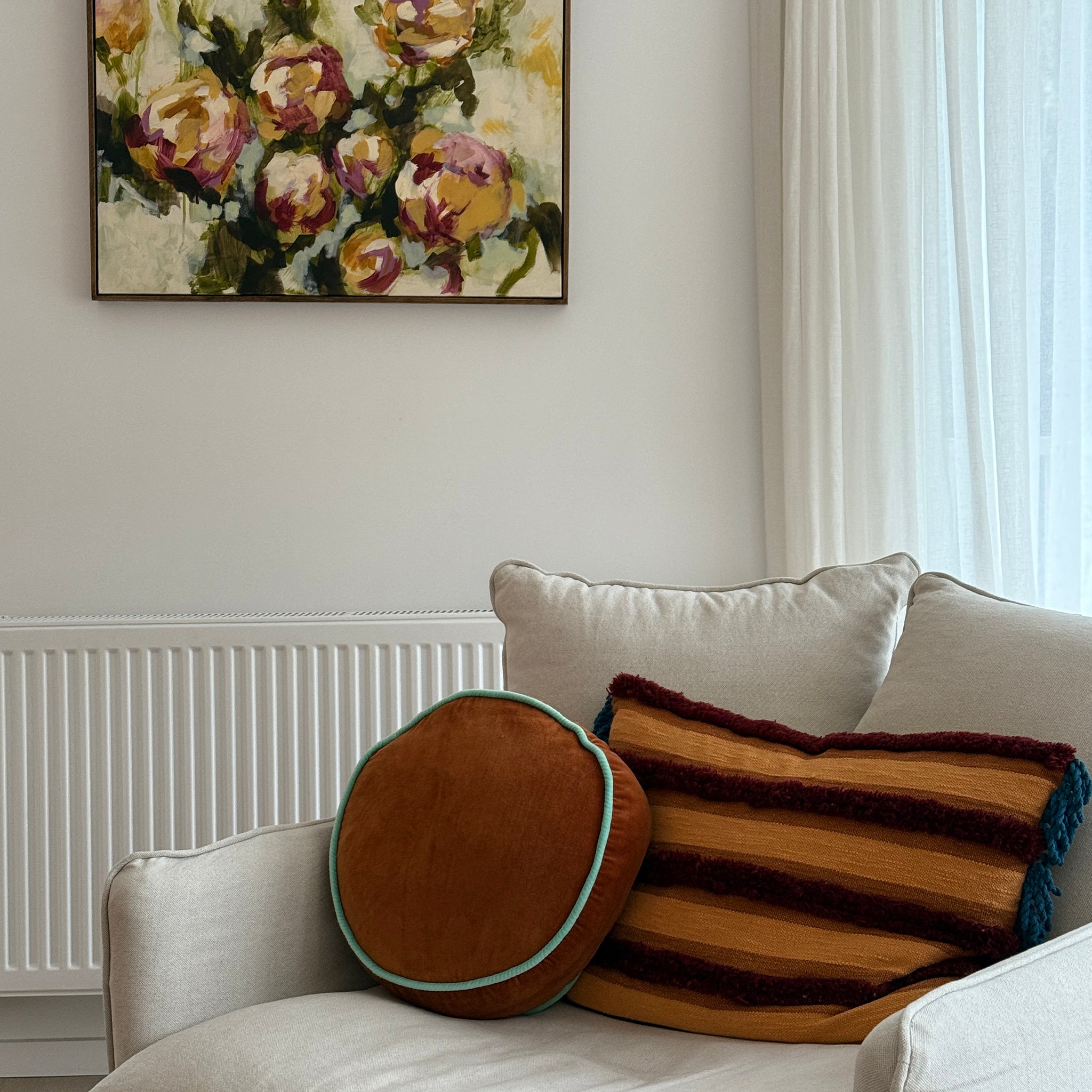 Decorative pillows on a sofa with a floral painting above in a living room.
