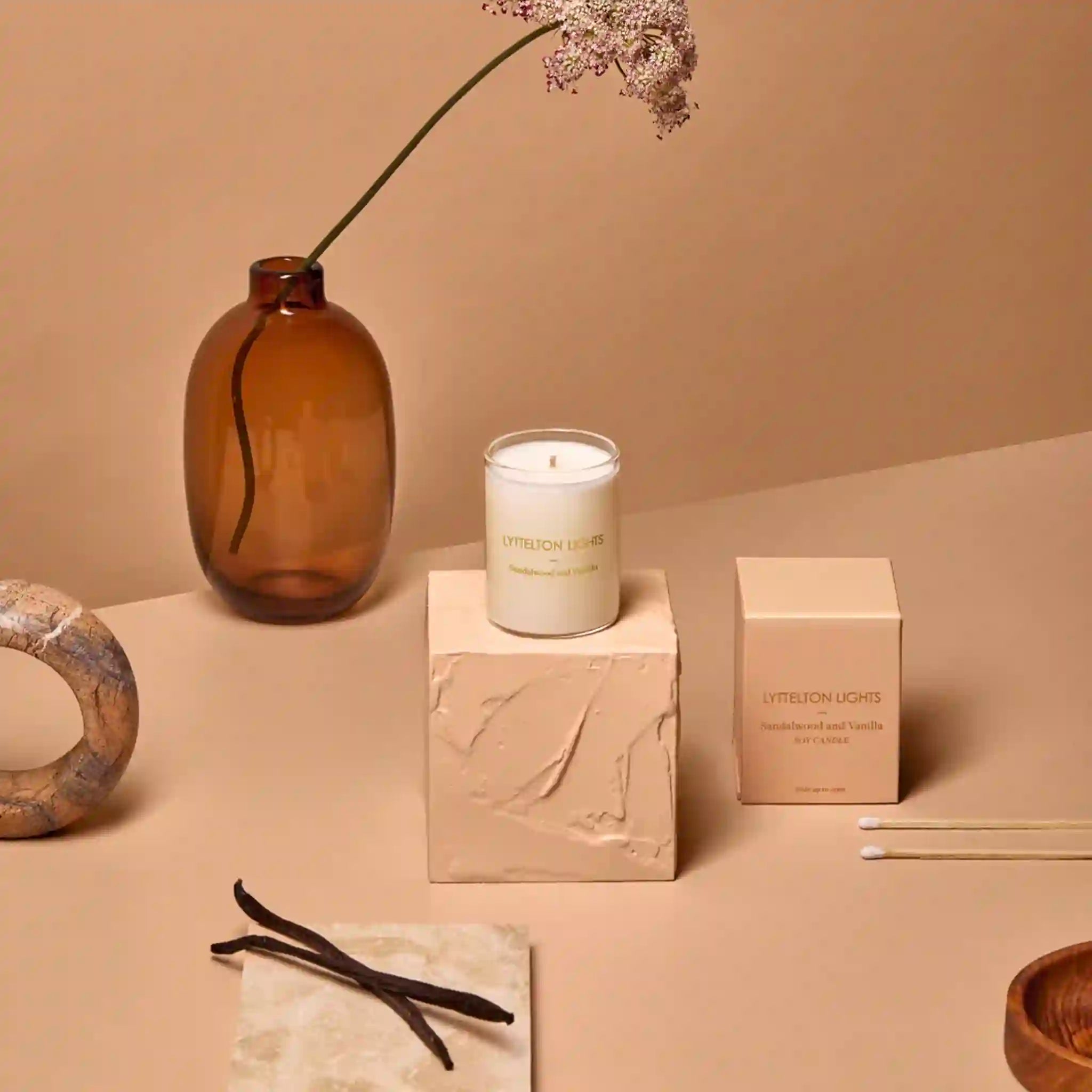 Candle with packaging and decorative items on a beige surface