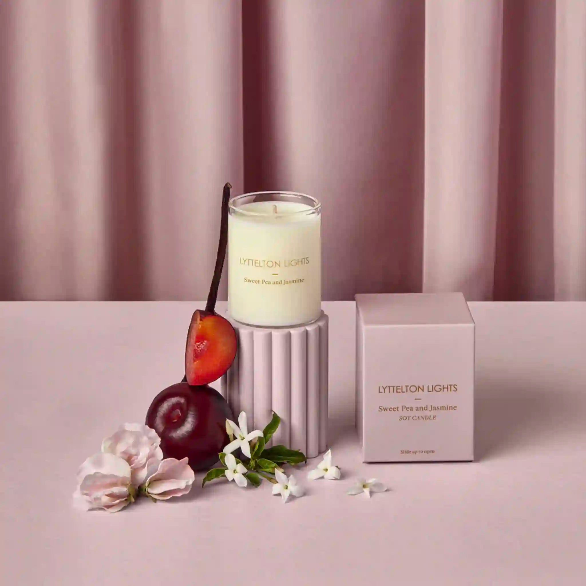 Candle with plums and flowers on a pink surface, with 'Lyttelton Lights' branding.