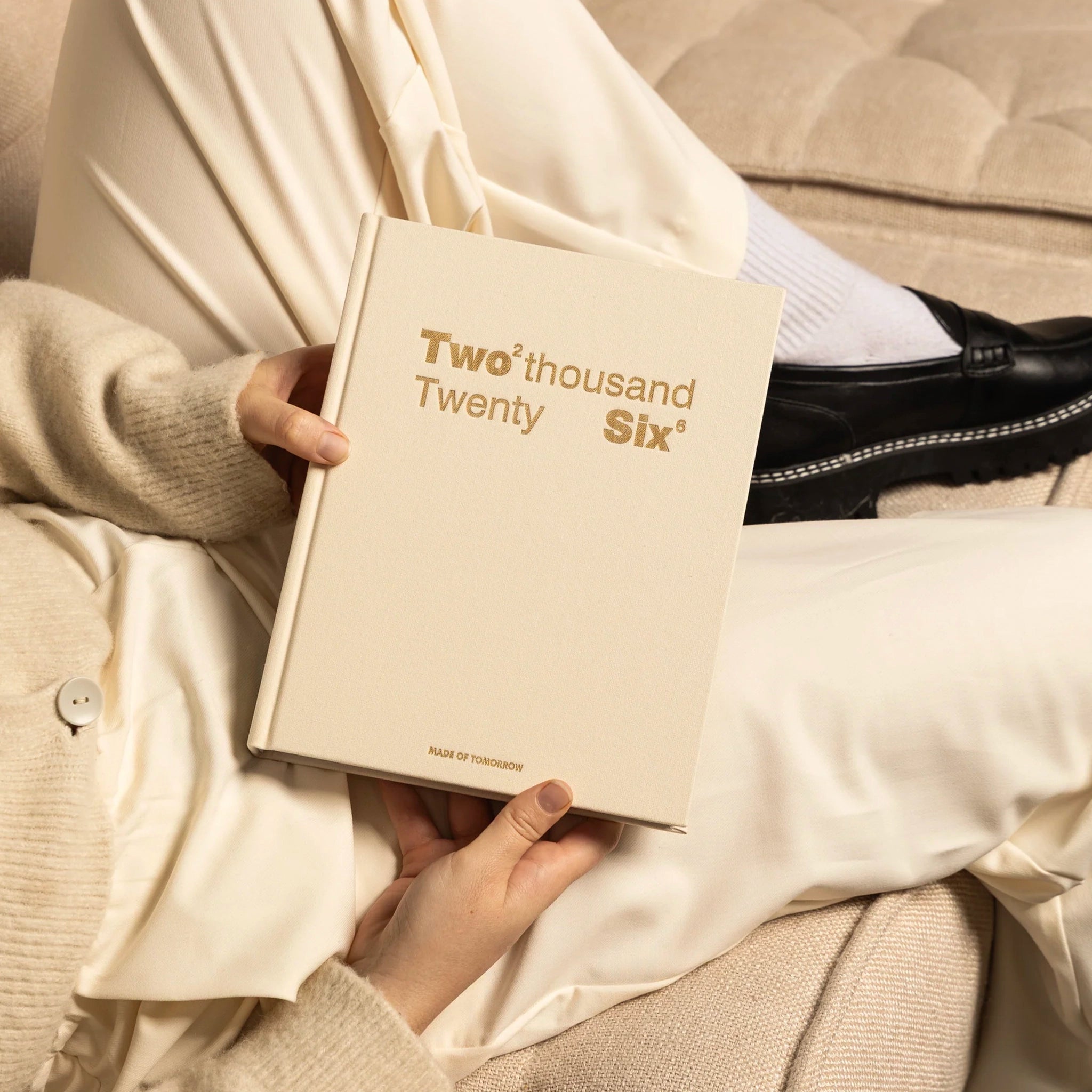 Person holding a beige book titled 'Two thousand Twenty Six' on a neutral background