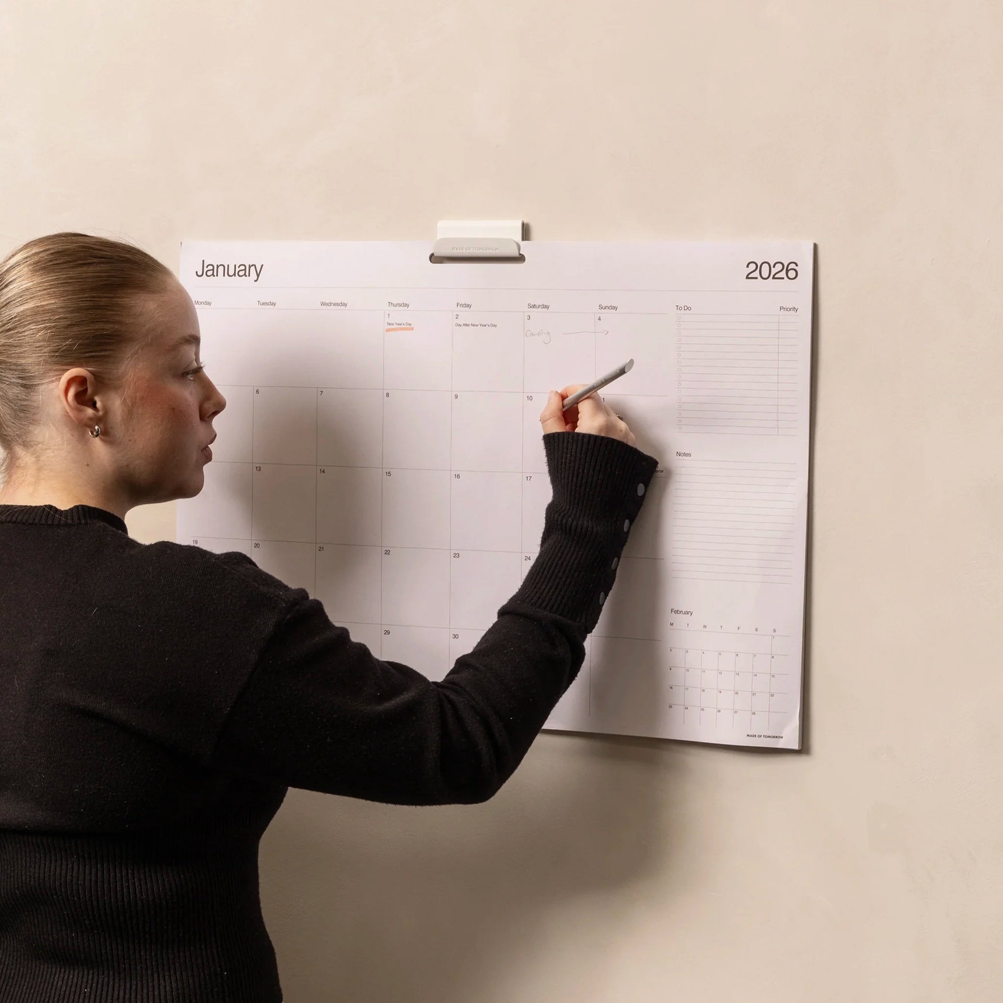 Person writing on a wall-mounted calendar for January 2026.