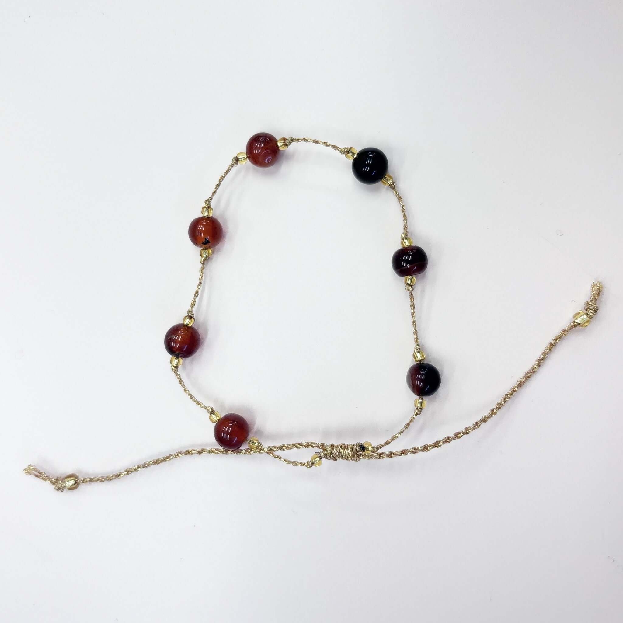 Margaret Loretta Bracelet featuring large round stone beads in carnelian red and garnet tones on a gold metallic cord.