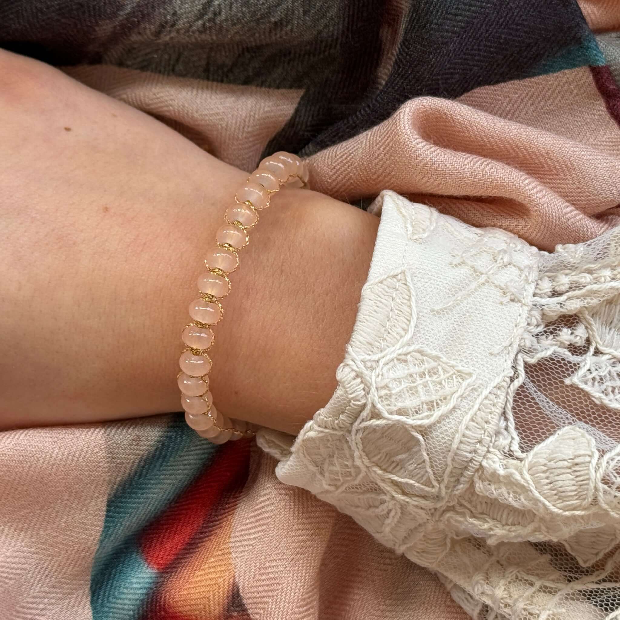 Margaret Edna Bracelet featuring chunky beads on gold metallic cord worn on a wrist with floral lace