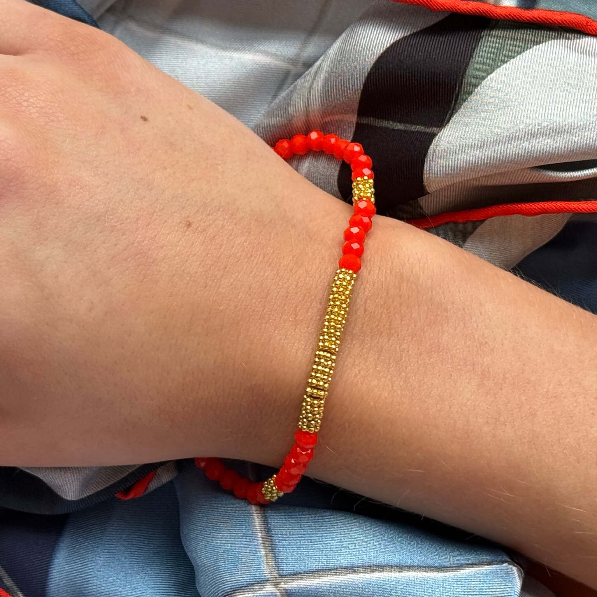 Margaret Lola Bracelet featuring red crystal beads and a woven gold bead centerpiece, styled on a wrist.