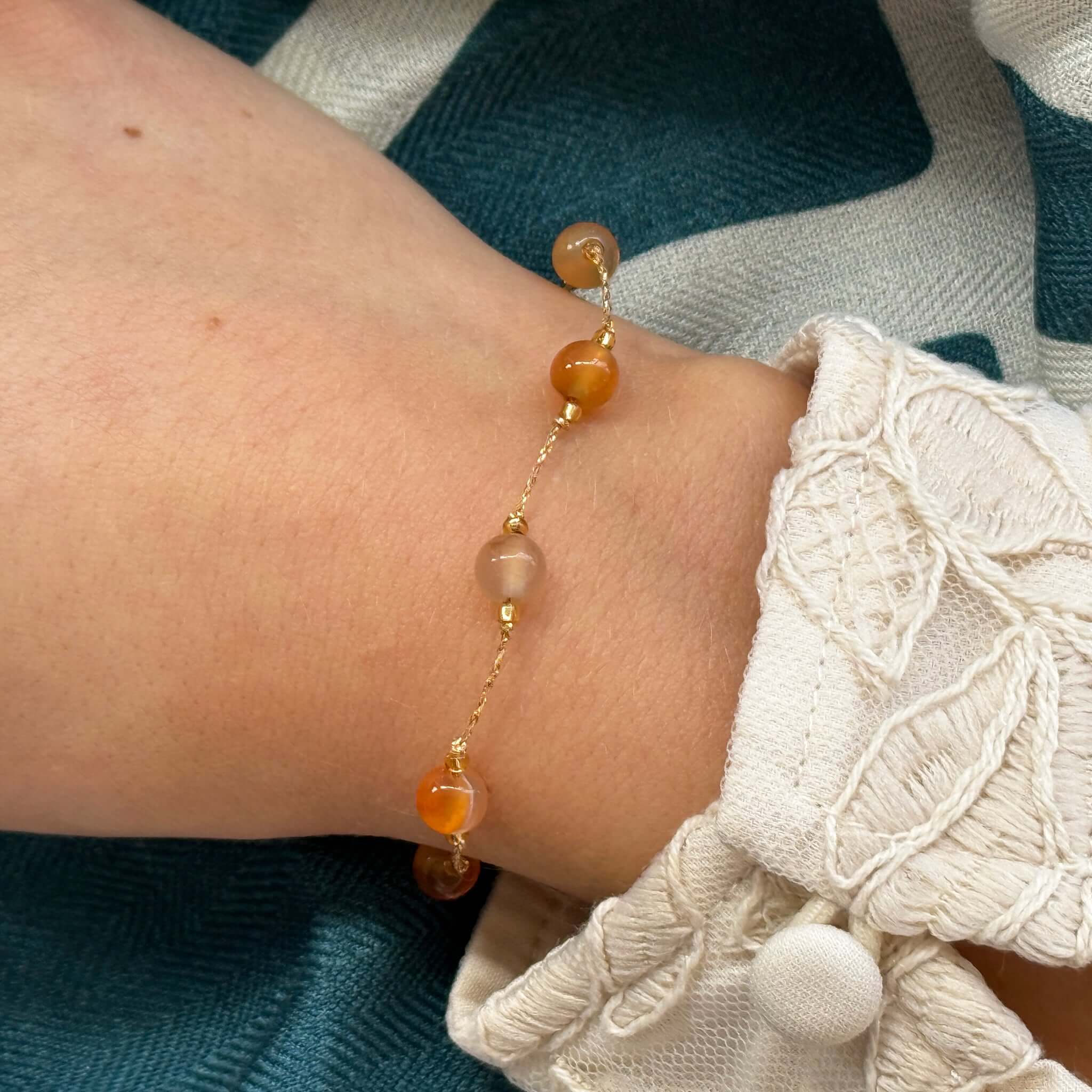 Close-up of a hand wearing the Margaret Loretta Bracelet featuring warm honey carnelian stones on a gold cord.