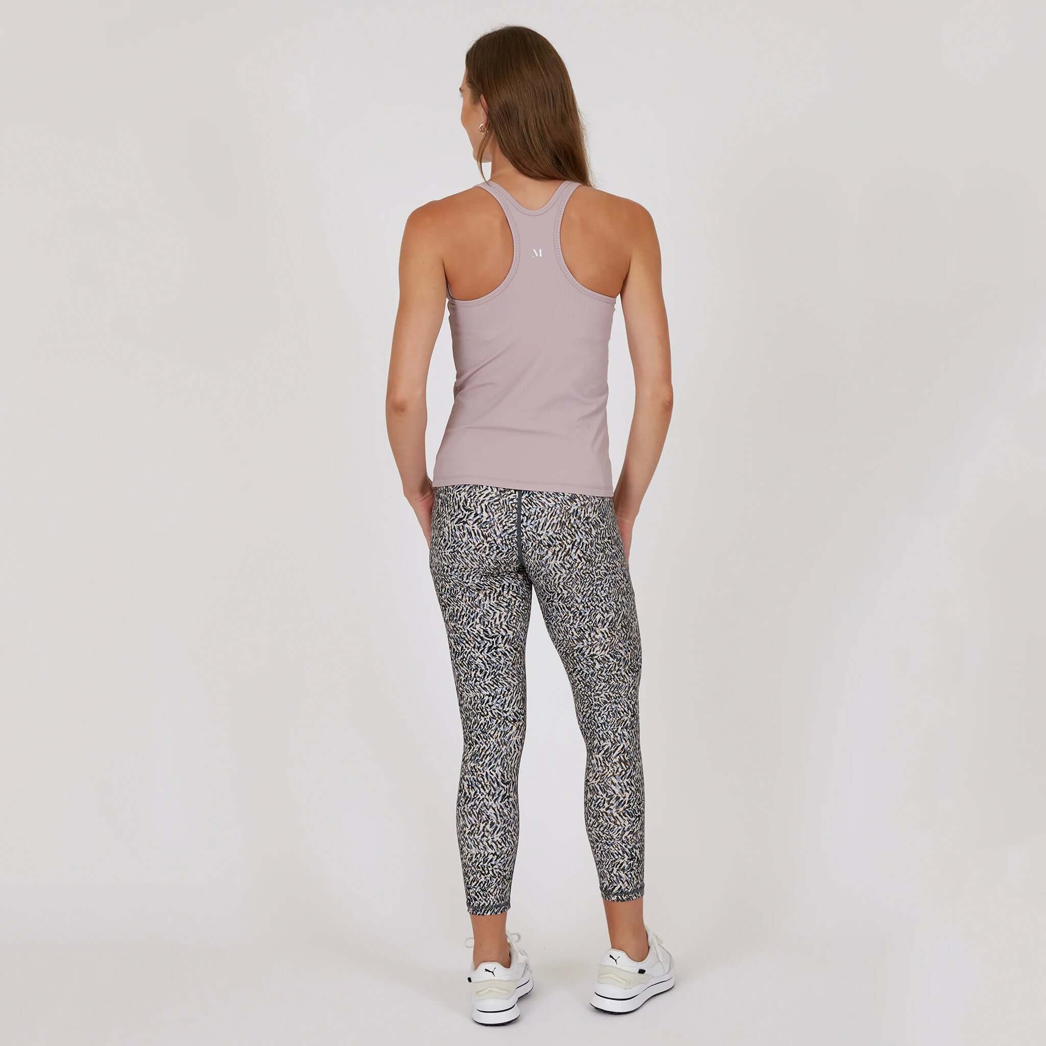 Rear view of a woman wearing the Marlow Contour Air Tank - Rose Beige with patterned leggings.