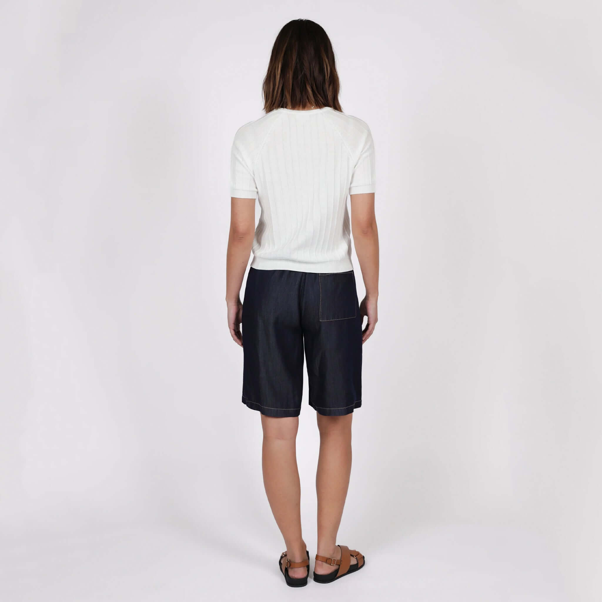 Back view of woman wearing Marlow Soleil Knit Tee - Ivory with denim shorts and sandals.