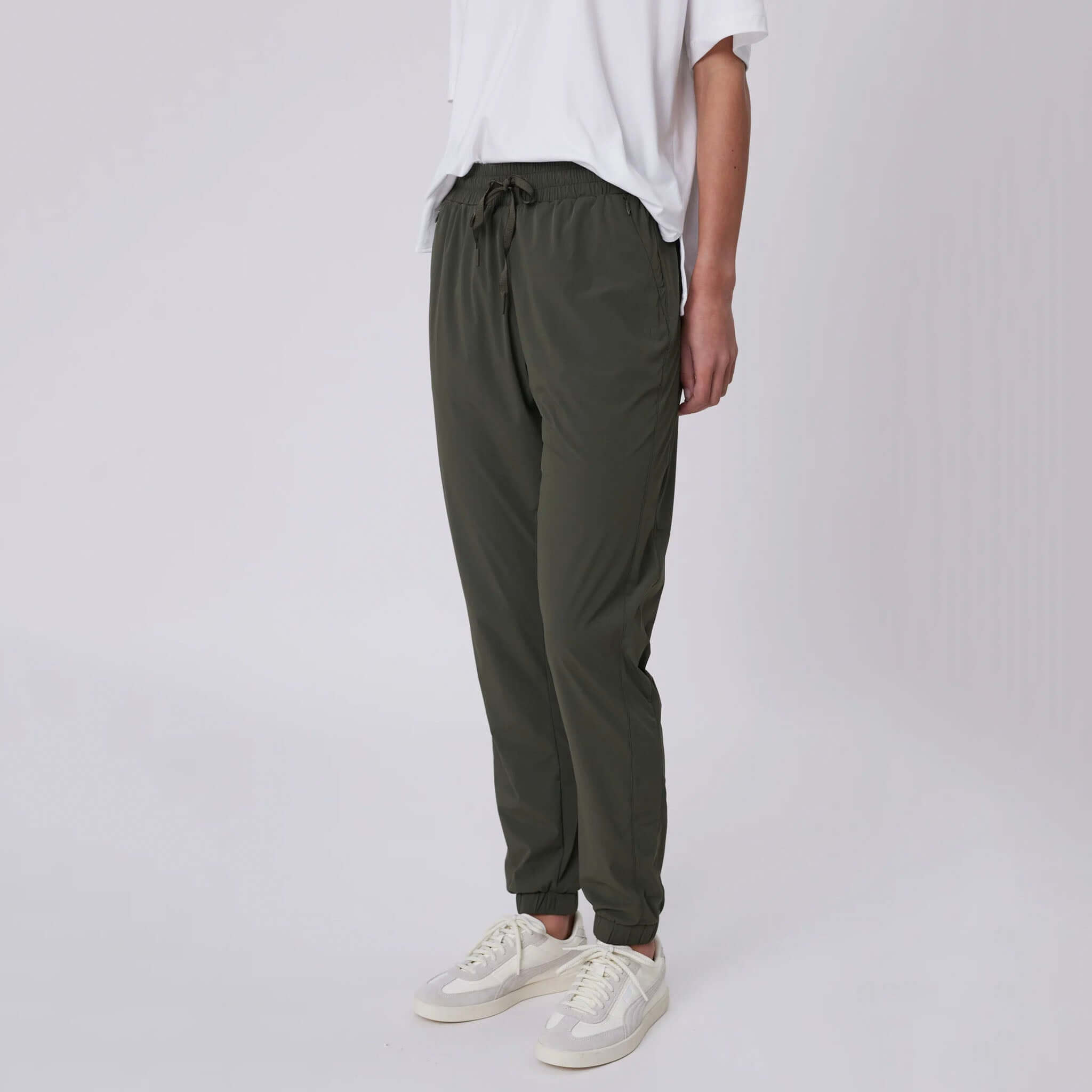 Alt Tag: Marlow Travel Pants - Olive on model, tapered leg featherlight stretch pants with drawstring waist and zip pockets