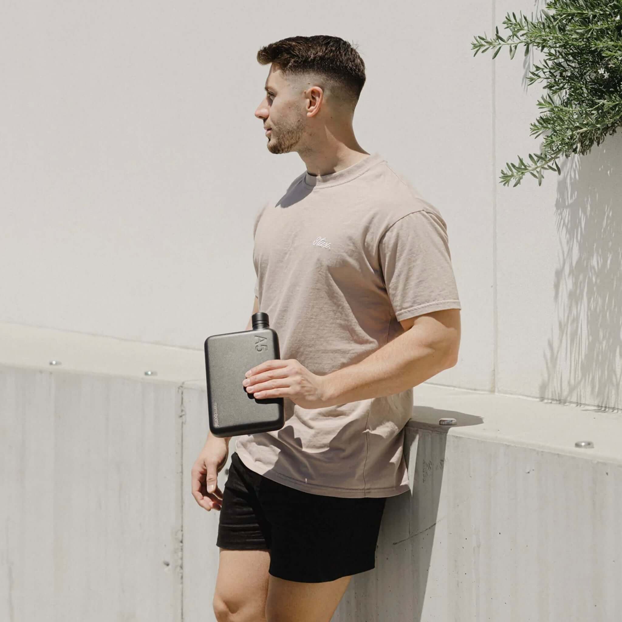 Alt Tag: Man holding Memobottle A5 Stainless Steel - Black flat water bottle outdoors, slim space-saving design