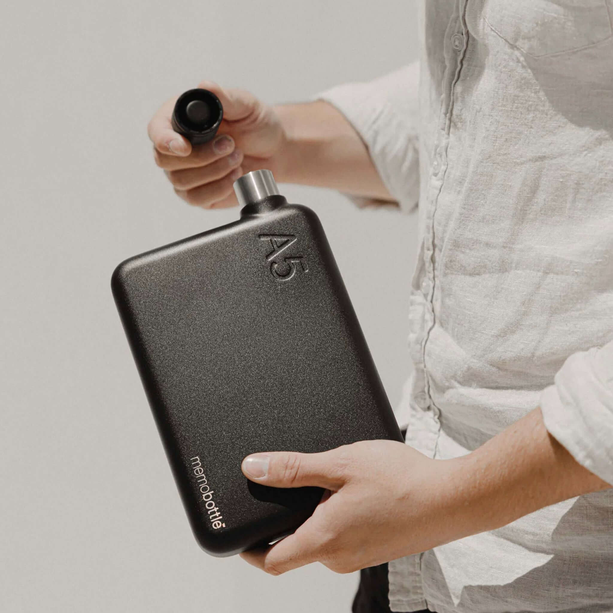 Alt Tag: Memobottle A5 Stainless Steel - Black flat stainless steel water bottle in hand, space-saving A5 design with wide opening