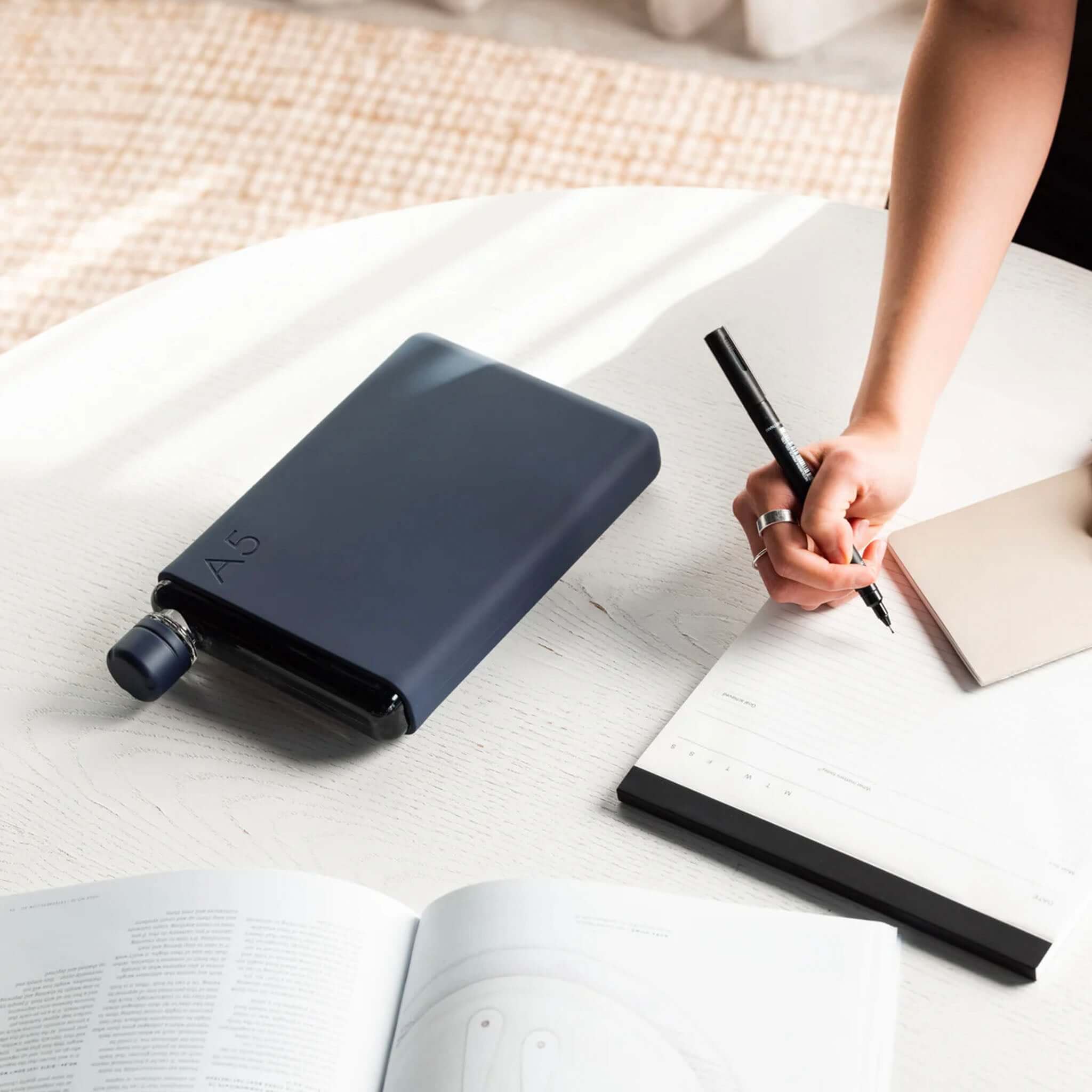 Memobottle Bundle A5 - Black Ink flat water bottle with matching sleeve and lid on desk beside notebook and pen