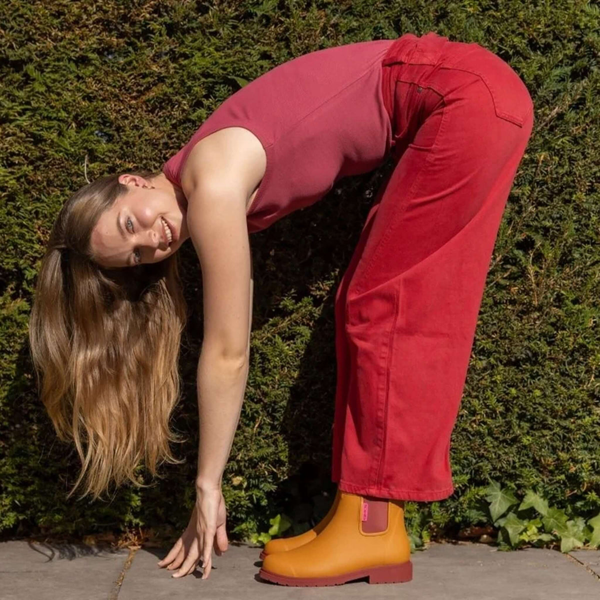 Merry People Bobbi Ankle Boots - Ochre worn by a woman in a red outfit, bending down while smiling outdoors.