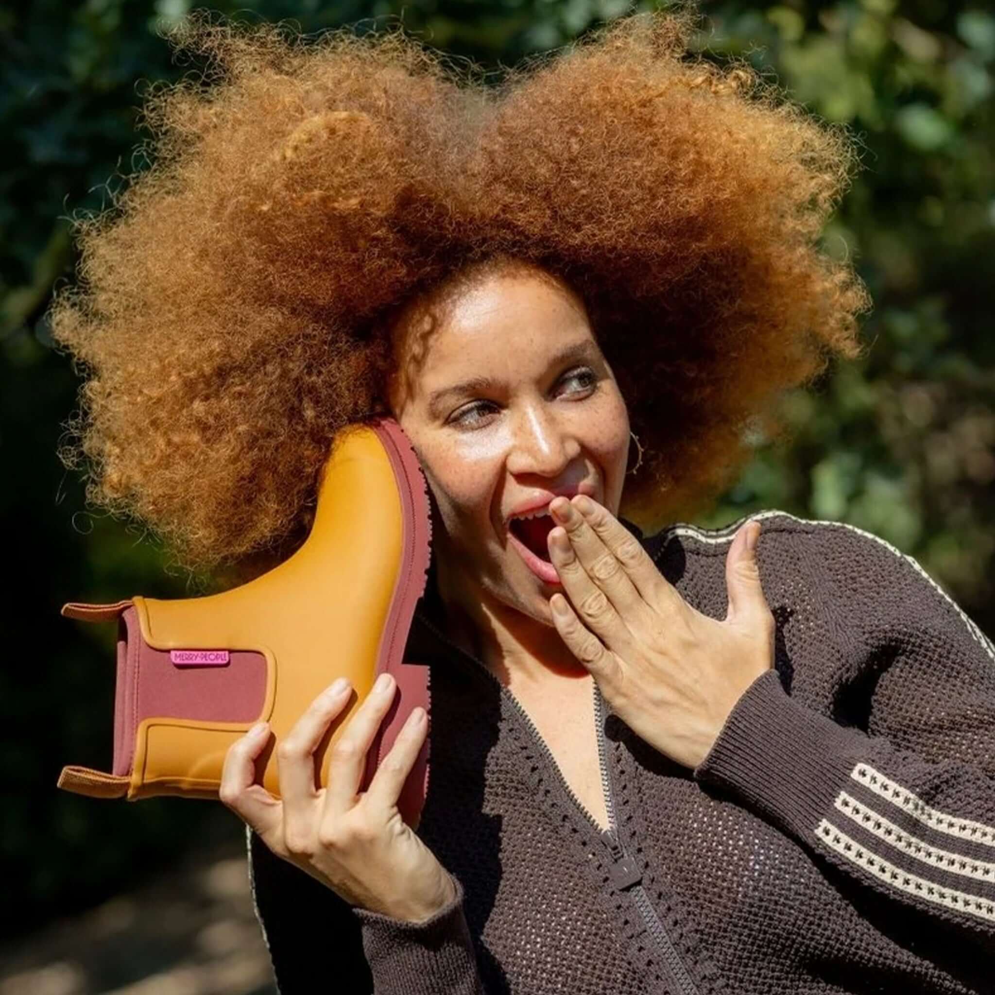 Merry People Bobbi Ankle Boots - Ochre held up by a smiling woman with curly hair outdoors.