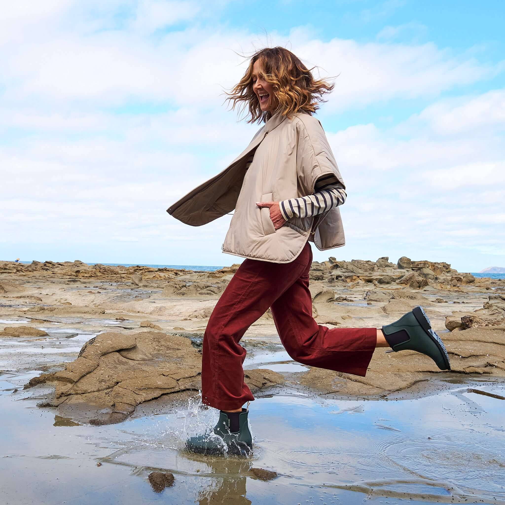 Woman joyfully splashing in puddles wearing Merry People Bobbi Ankle Boots - Forest Green and a stylish jacket.